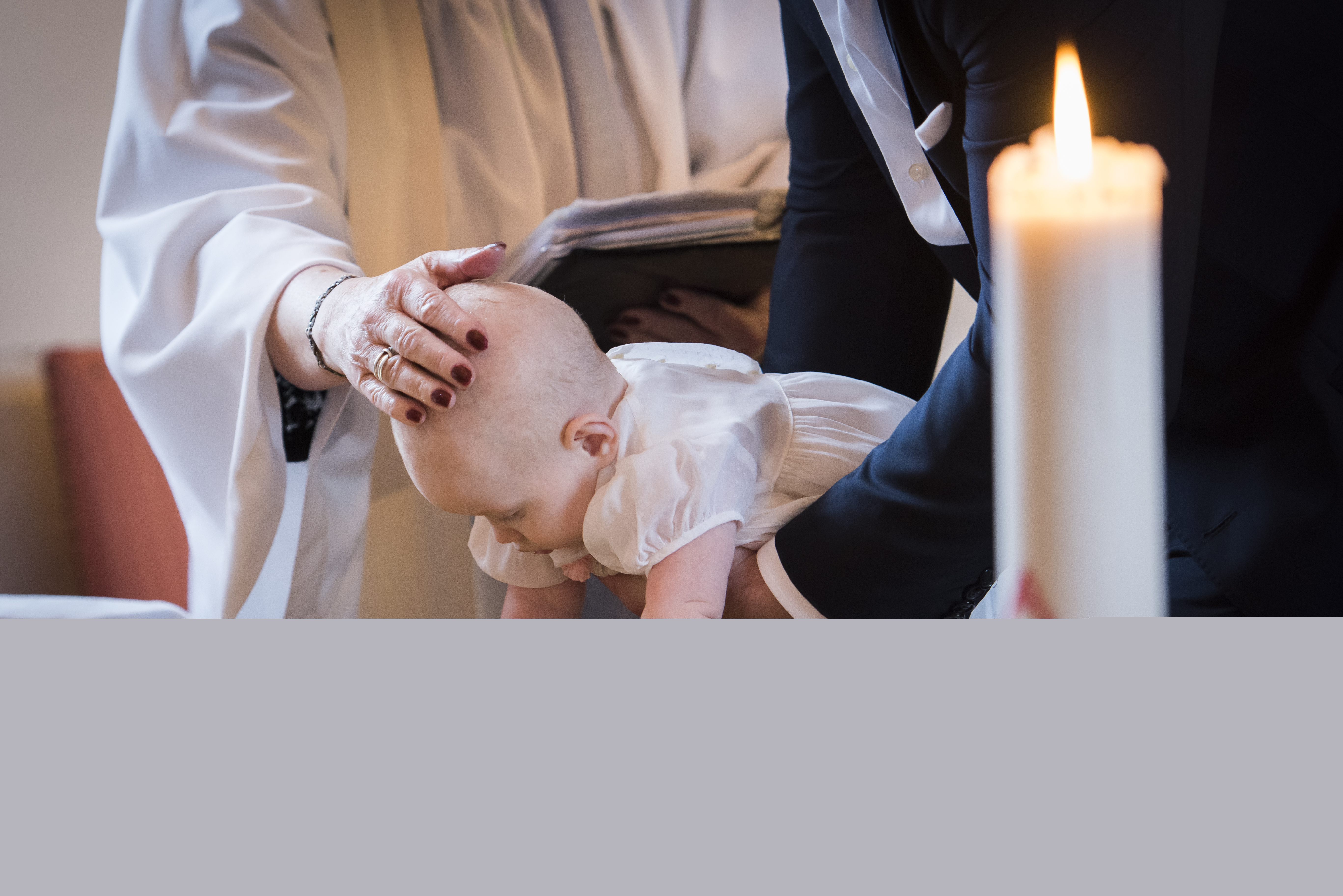 Någon sänker en bebis ner i dopfunten medan prästen håller sin hand på barnets huvud.