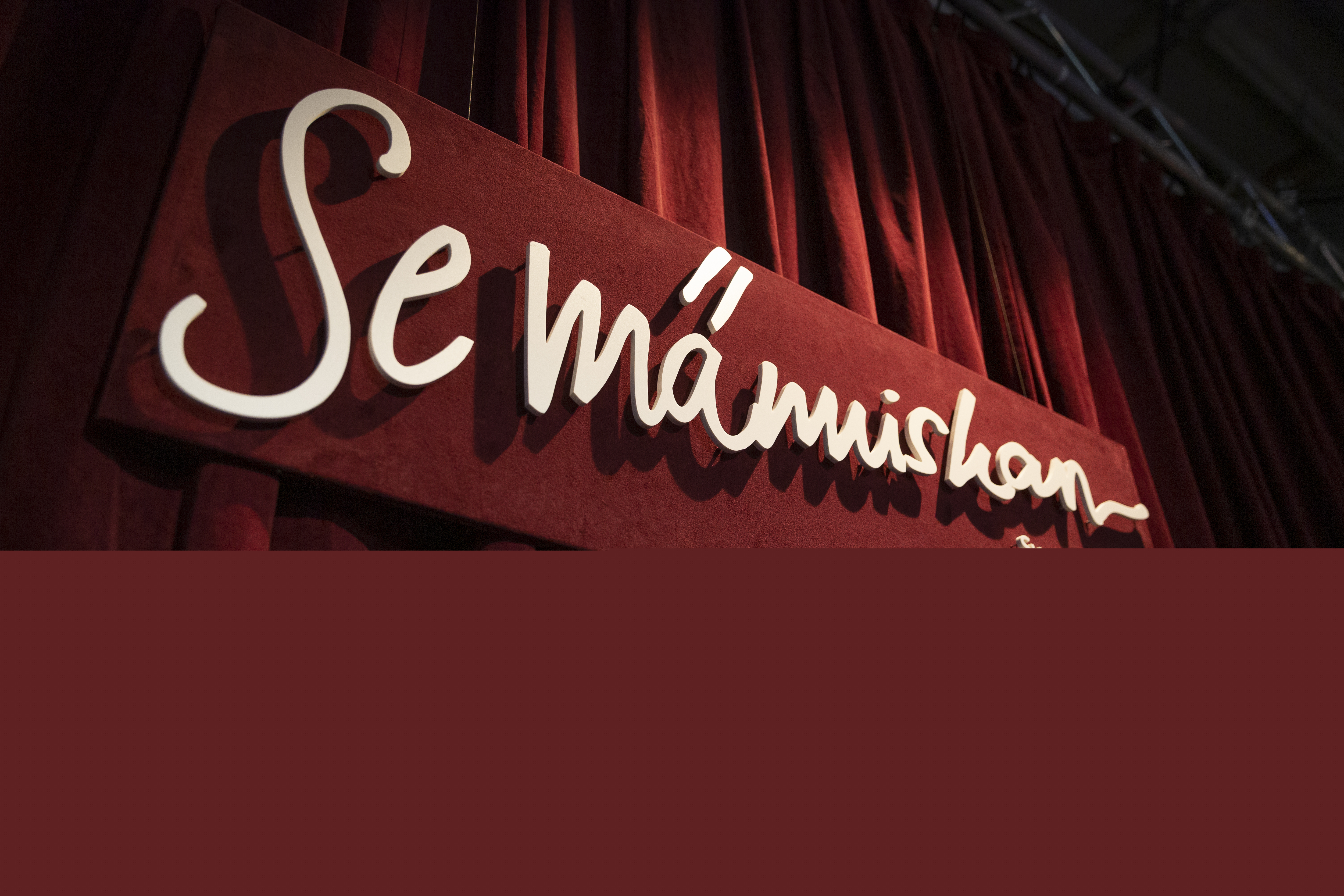 Framför ett rött draperi hänger en skylt med texten Se människan.