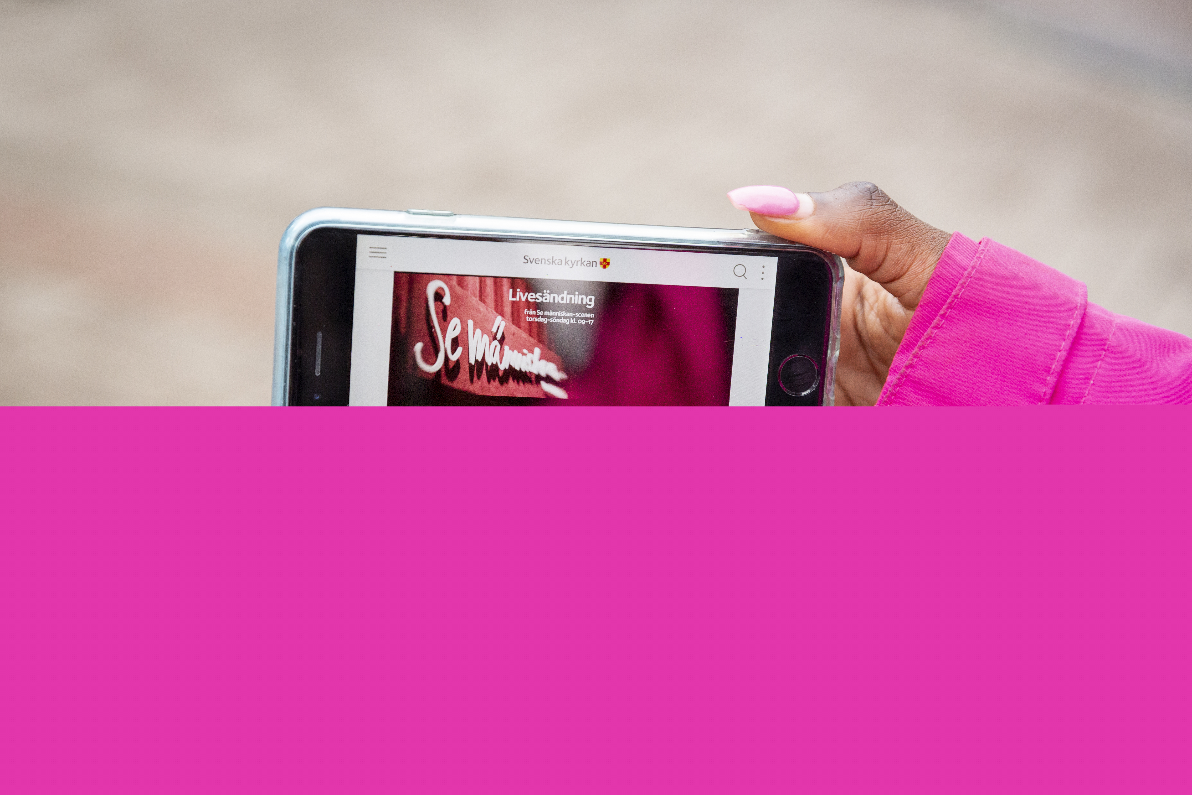 Ett par händer håller upp en mobil som visar en bild med texten Se människan.