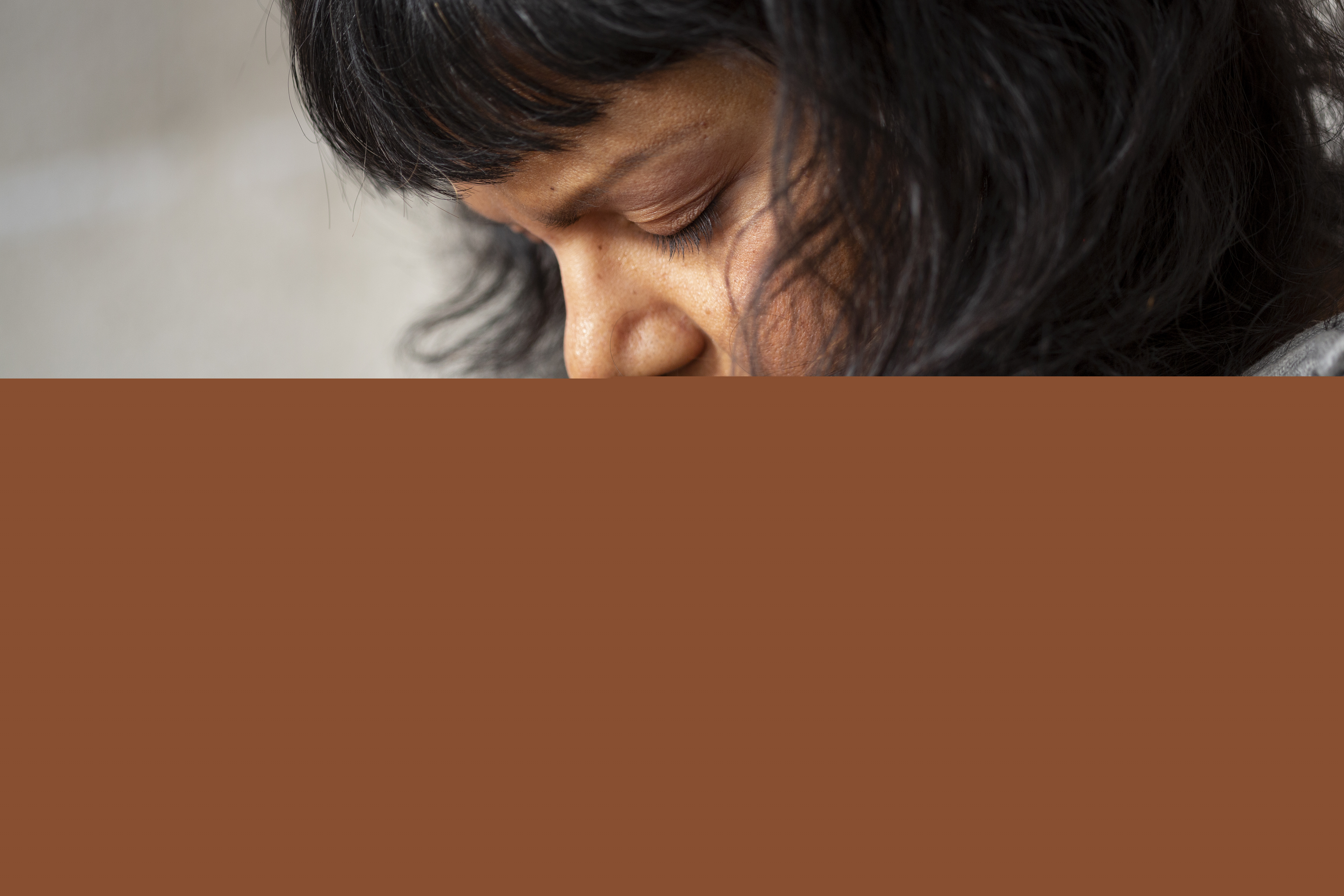 En kvinna som blundar har fört sina knäppta händer till sitt ansikte.