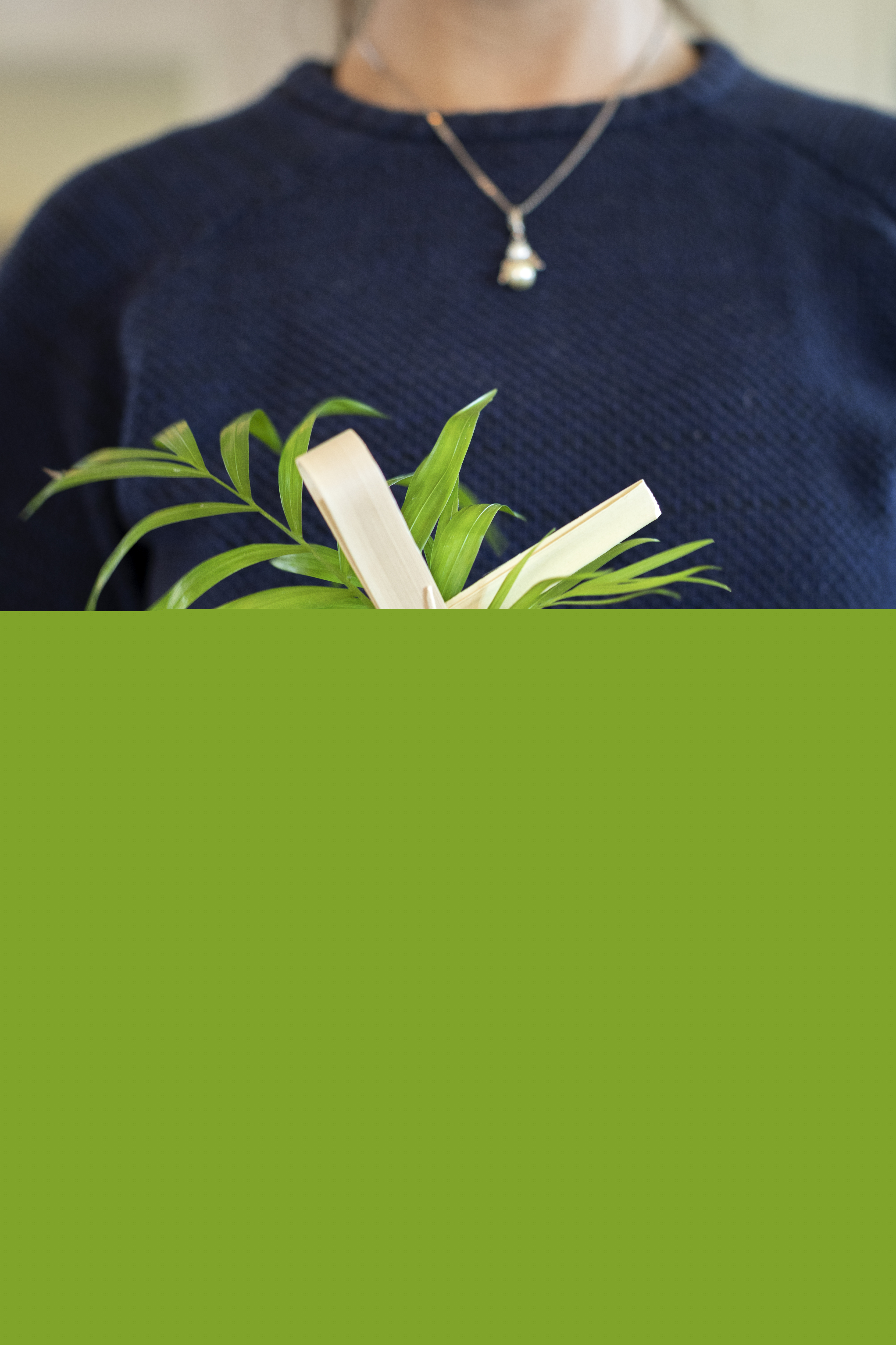 Någon håller ett träkors med fastknutna palmblad.