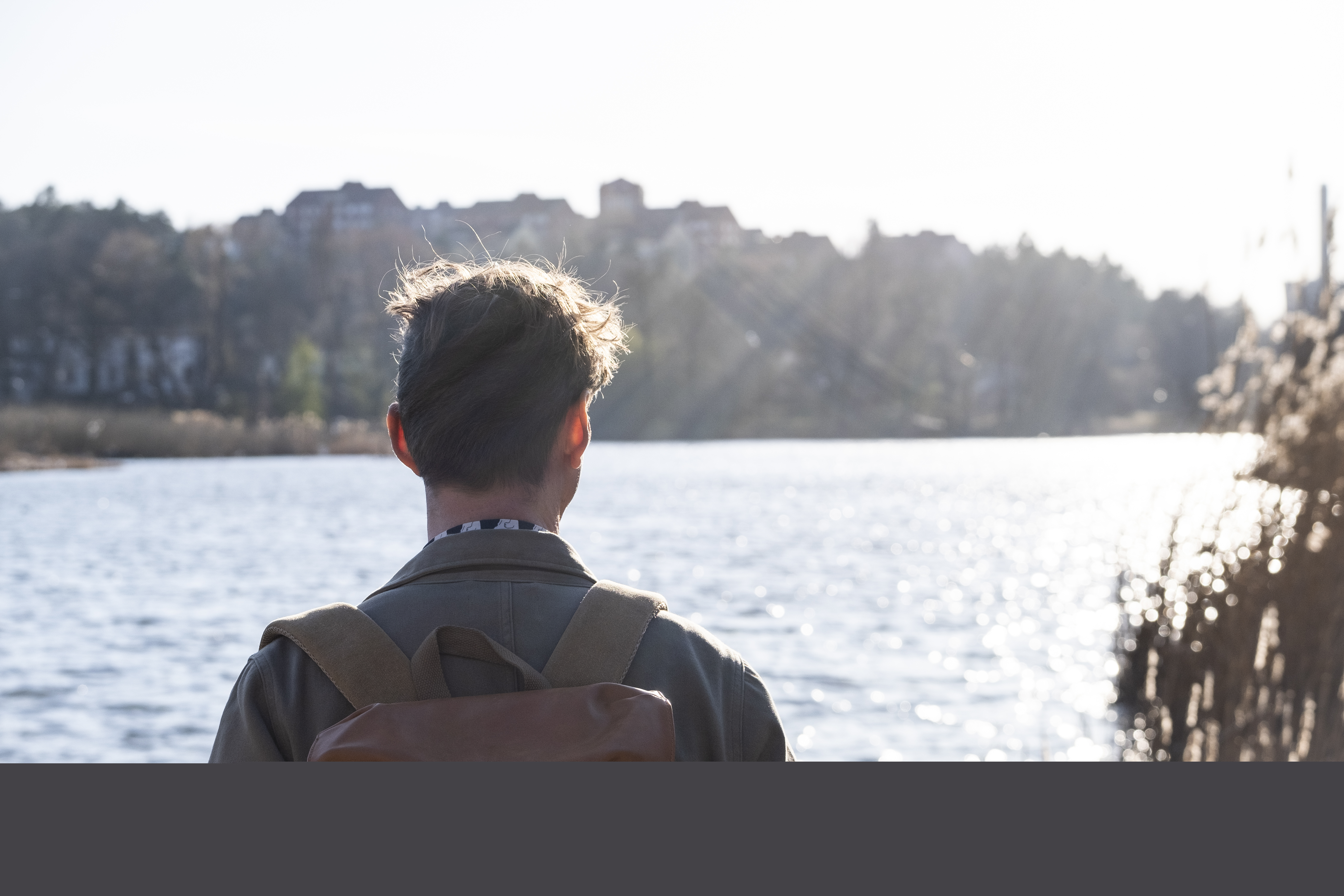 En man med ryggsäck tittar ut över vattnet i solen.