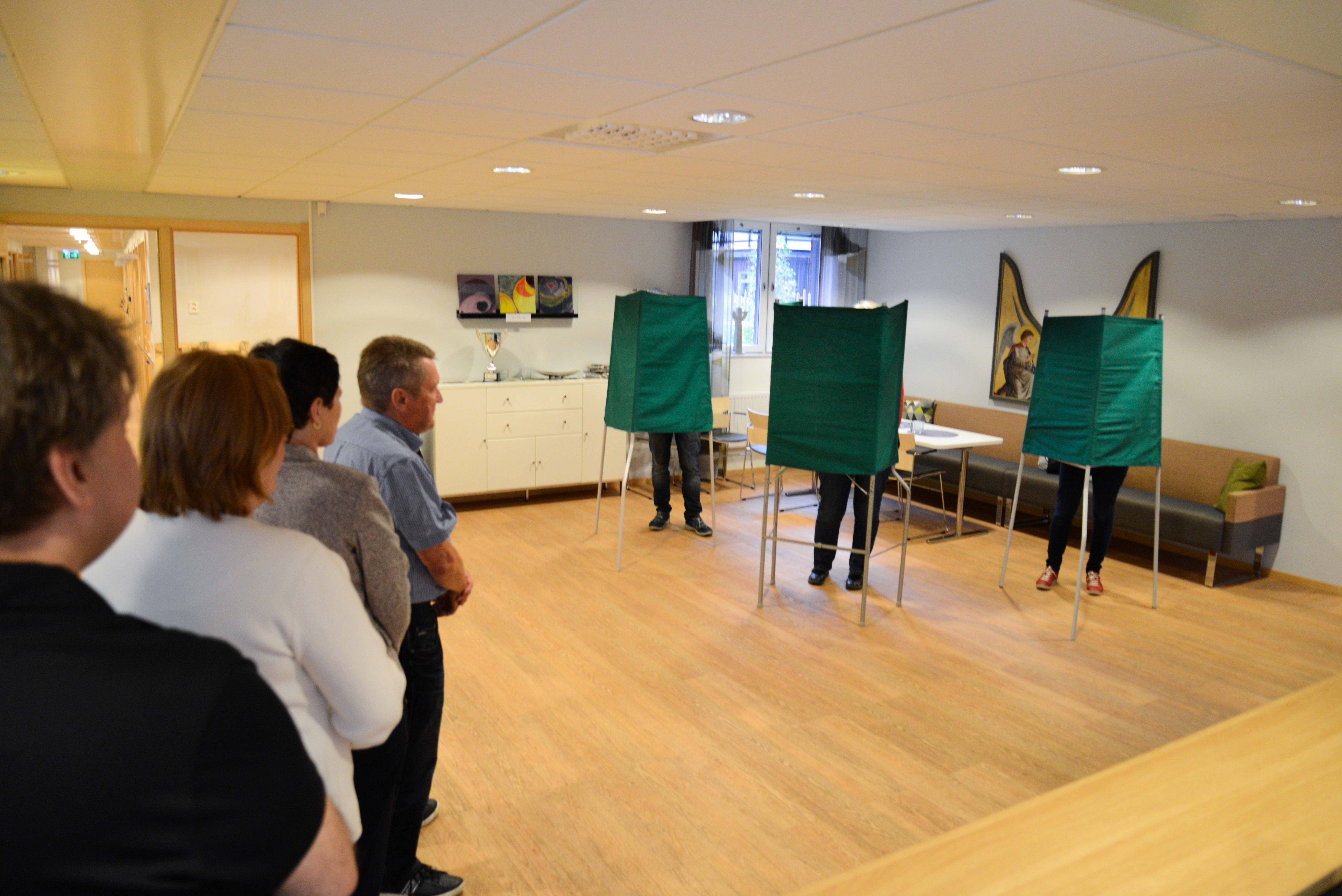 Några personer står i kö i en vallokal.