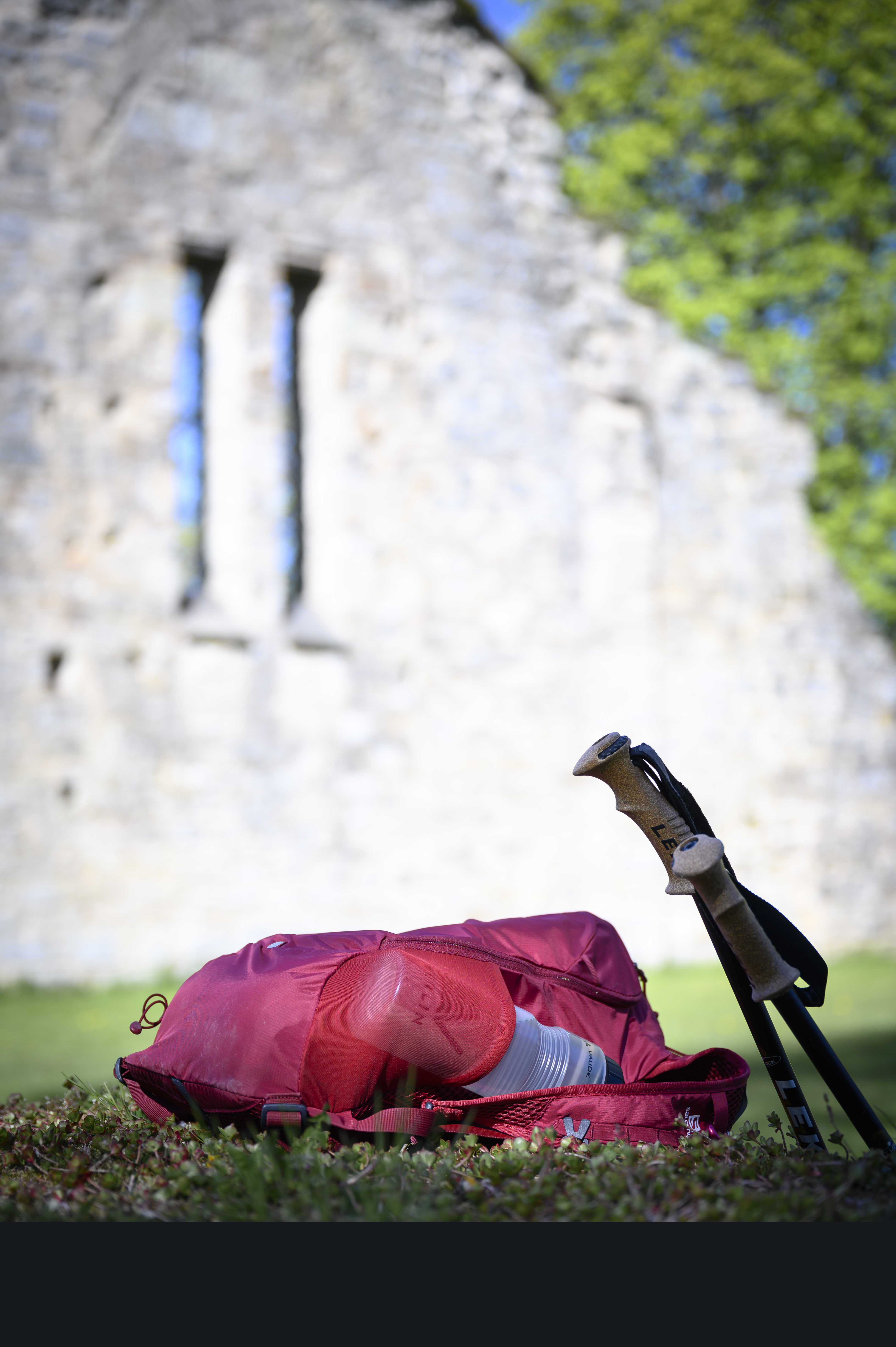 Ett par vandringsstavar och en liten ryggsäck ligger på gräset framför en gammal ruin.