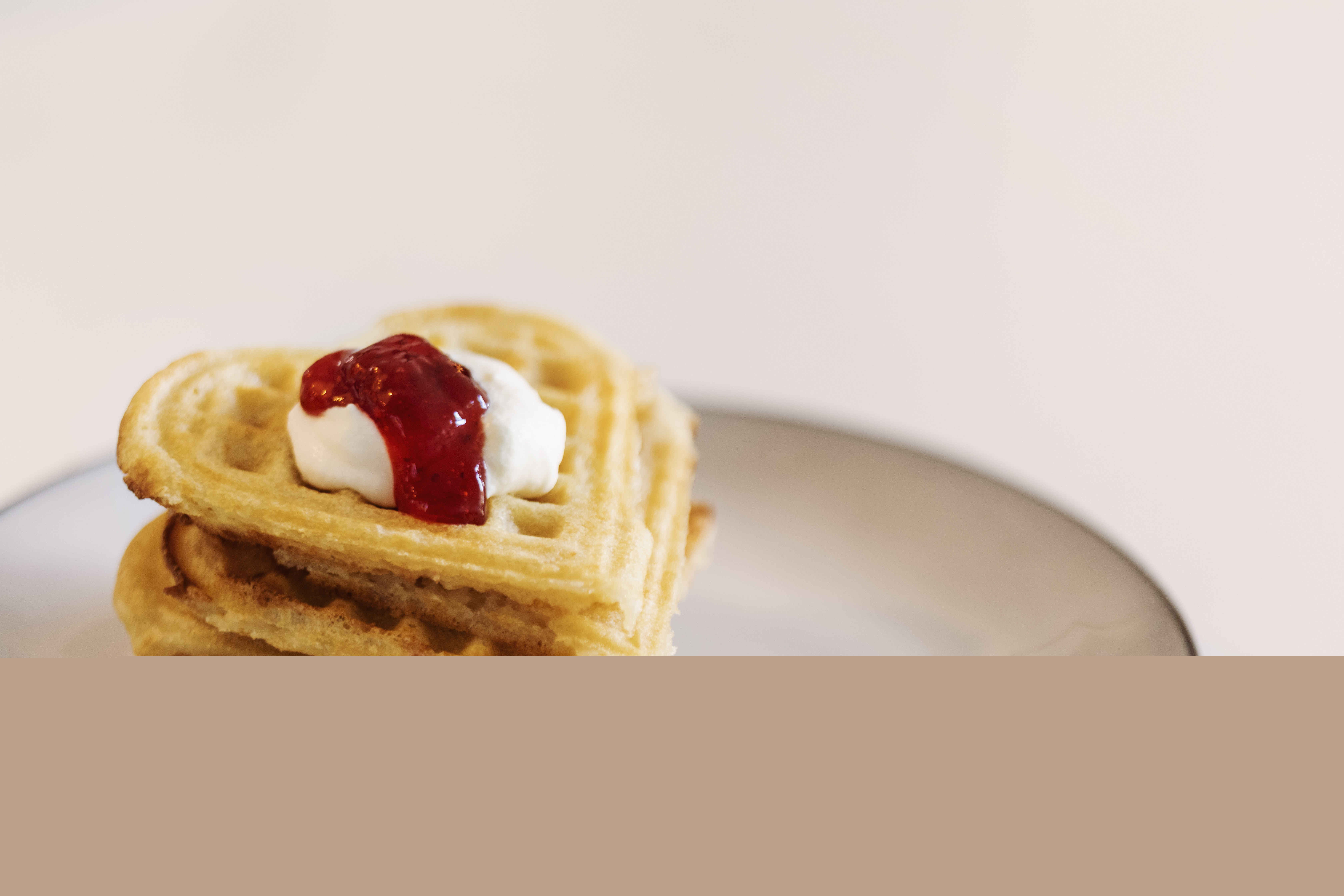 En stapel av hjärtformade våfflor på en tallrik, toppade med grädde och sylt.