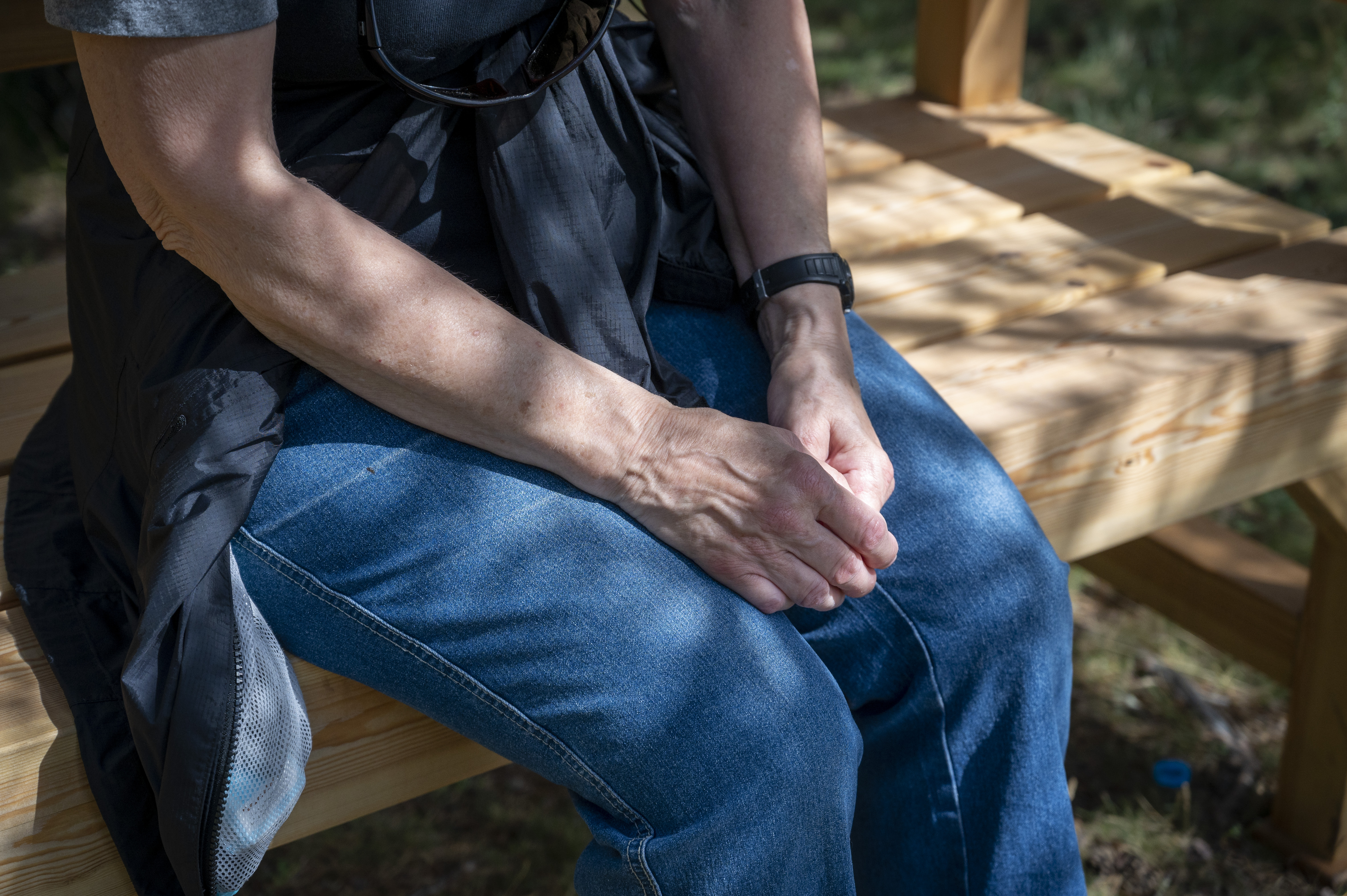 En person sitter på träbänk med händerna i knät.