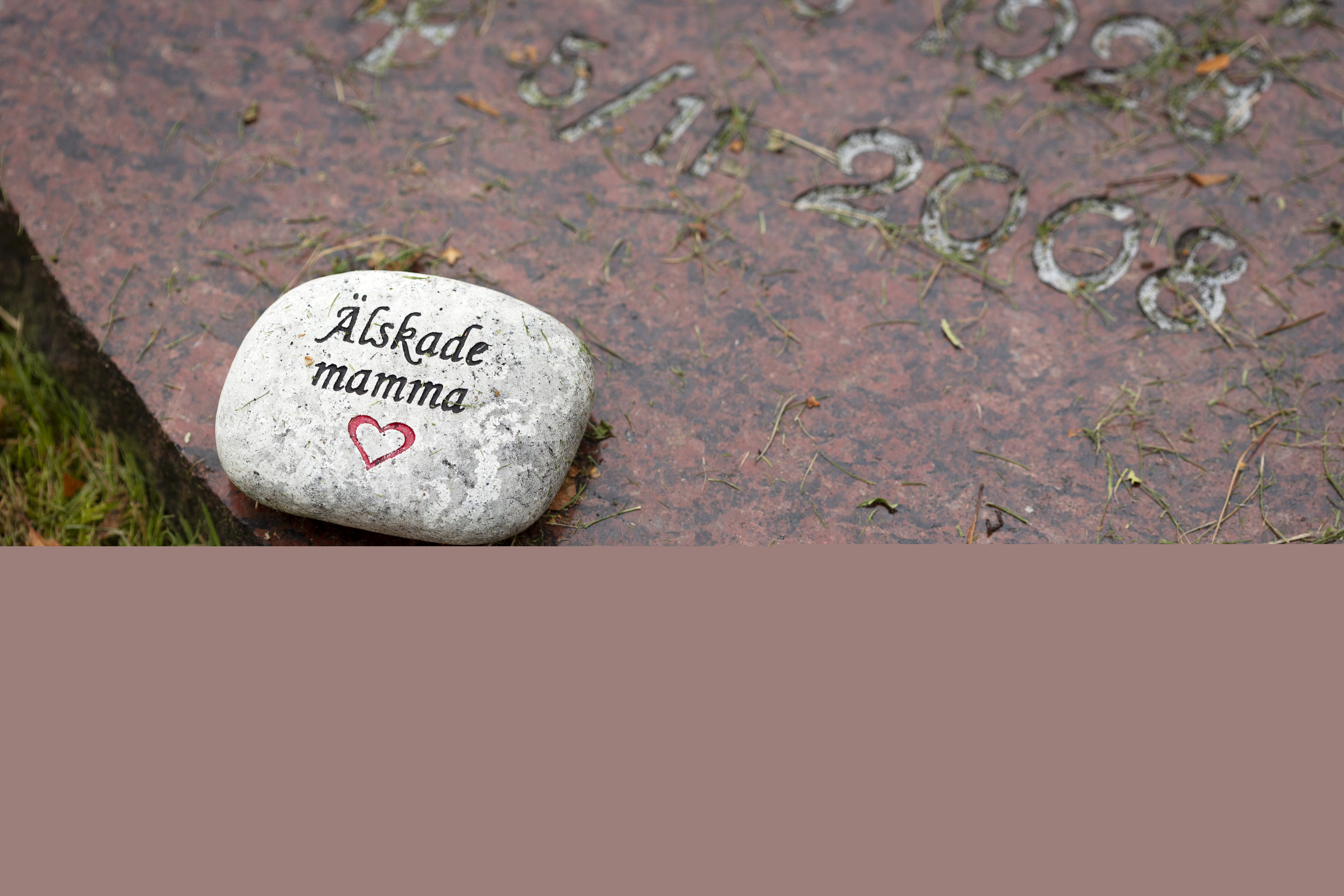 Liten sten med texten "älskade mamma" inristad ligger på en gravsten.