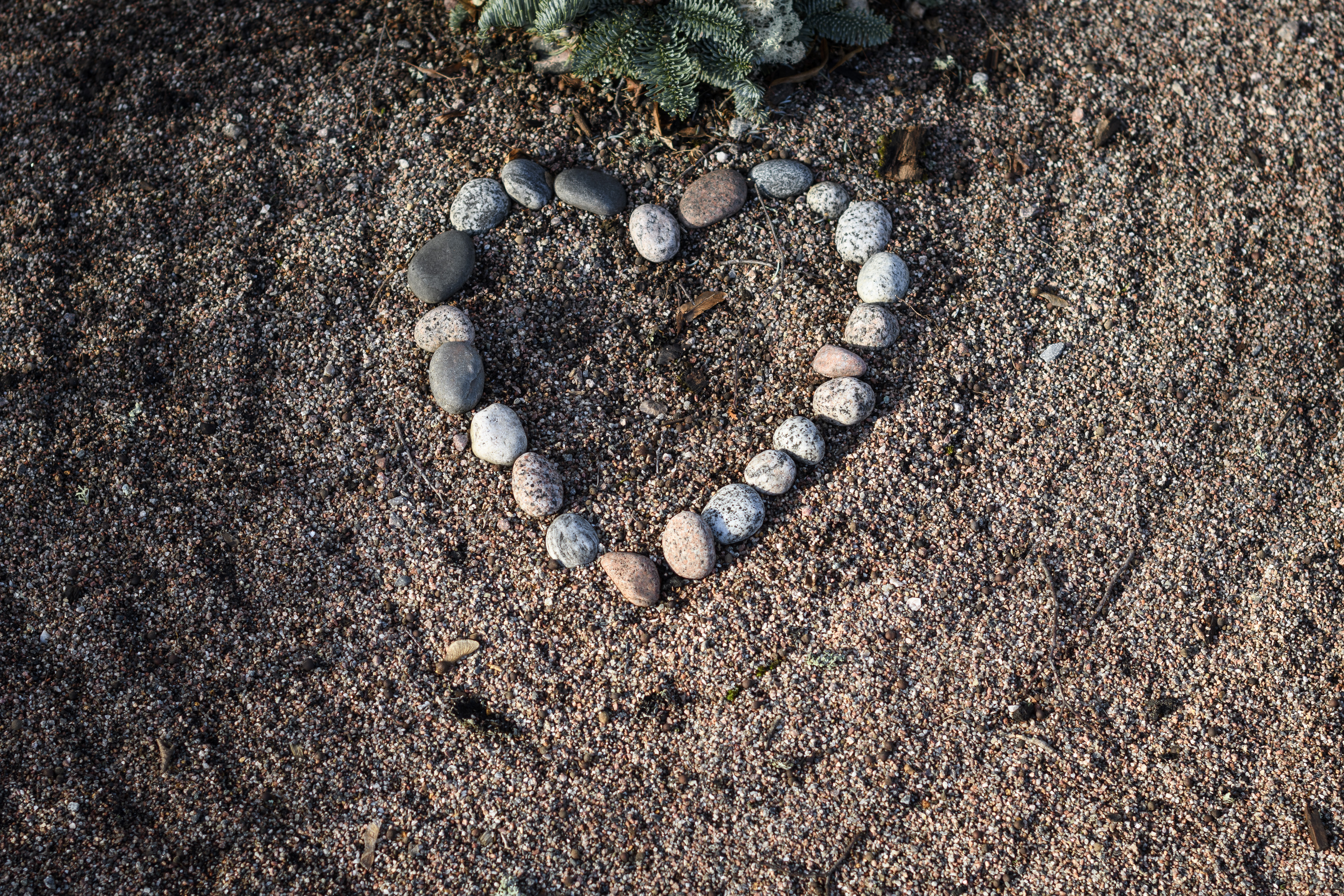 Stenar upplagda i form av ett hjärta framför en krans på en grav.