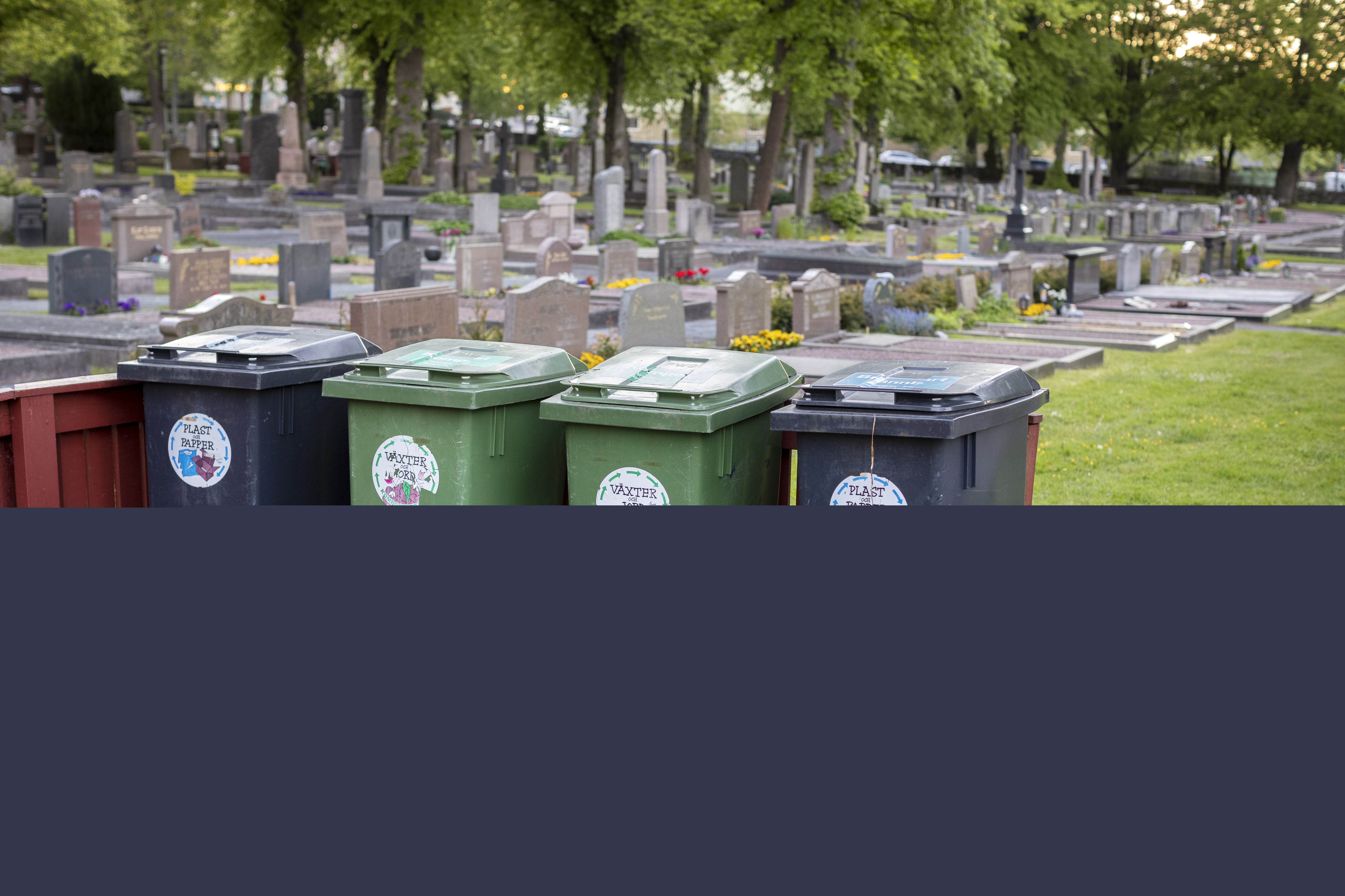 Tunnor för sopsortering står uppställda på en kyrkogård.