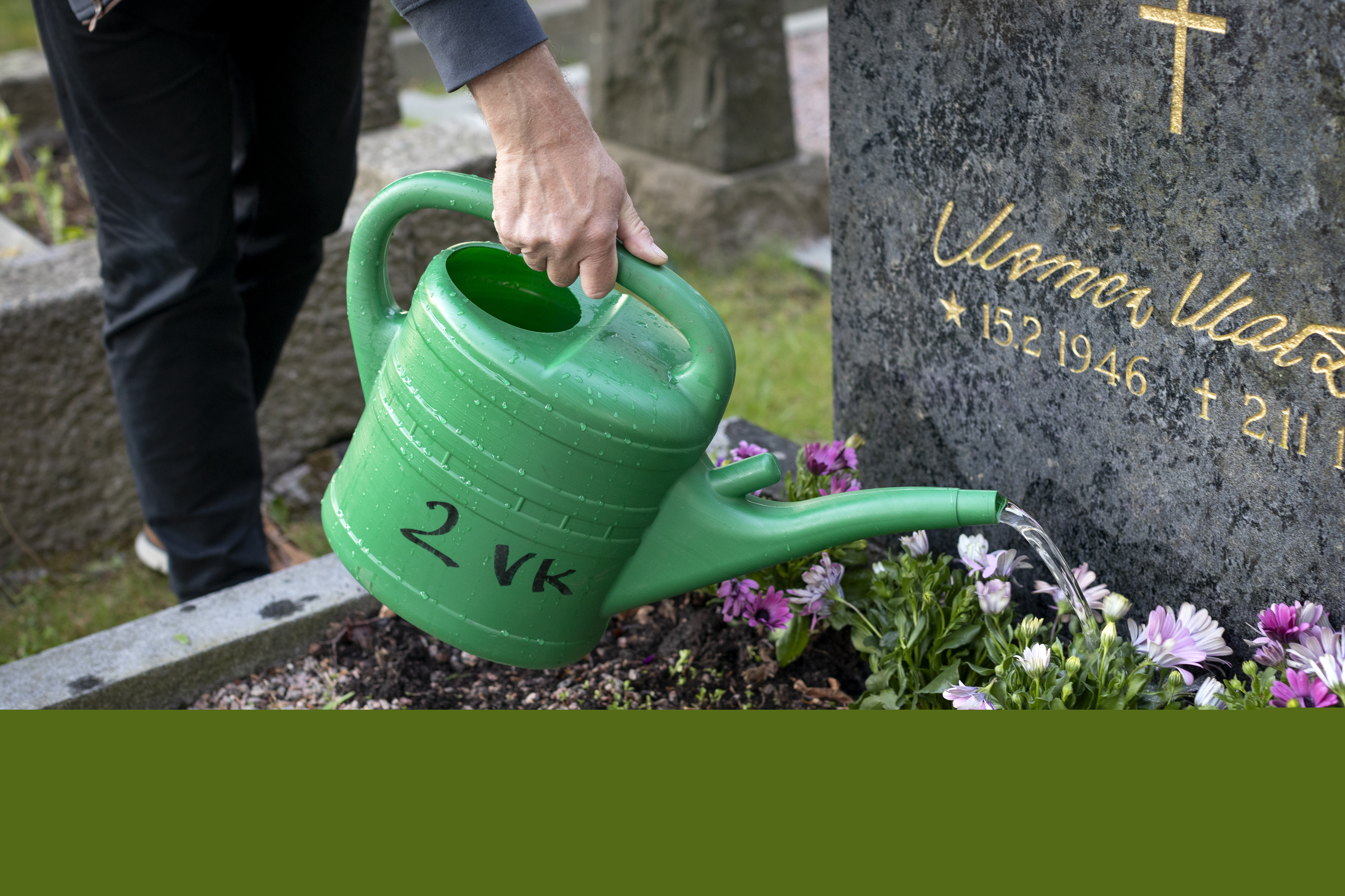 Någon vattnar blommorna på en grav.