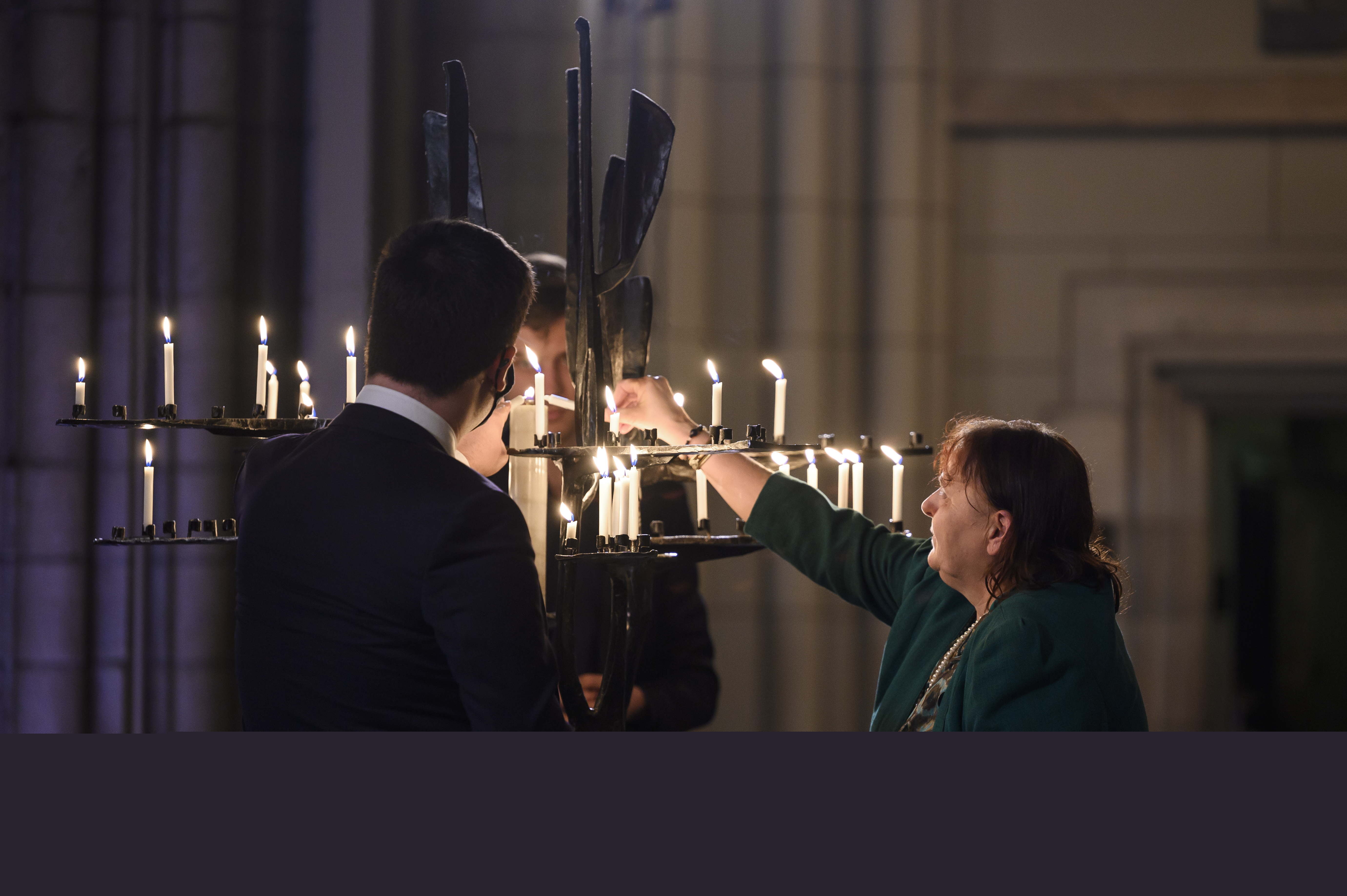 Några personer tänder ljus i järnskulpturen Folkförsoningens träd i Uppsala domkyrka.