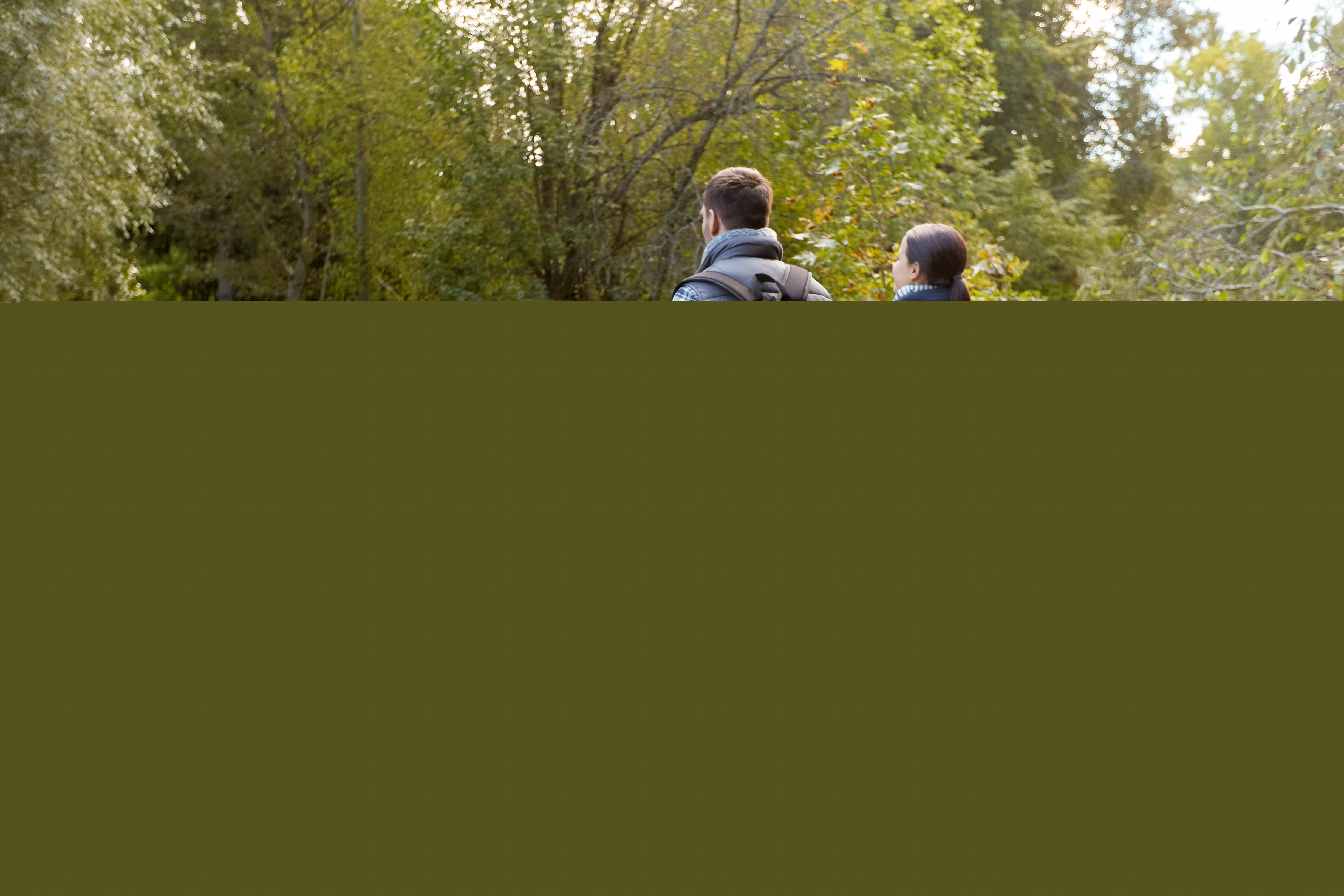En familj med två barn går hand i hand på en vandringsled i skogen.
