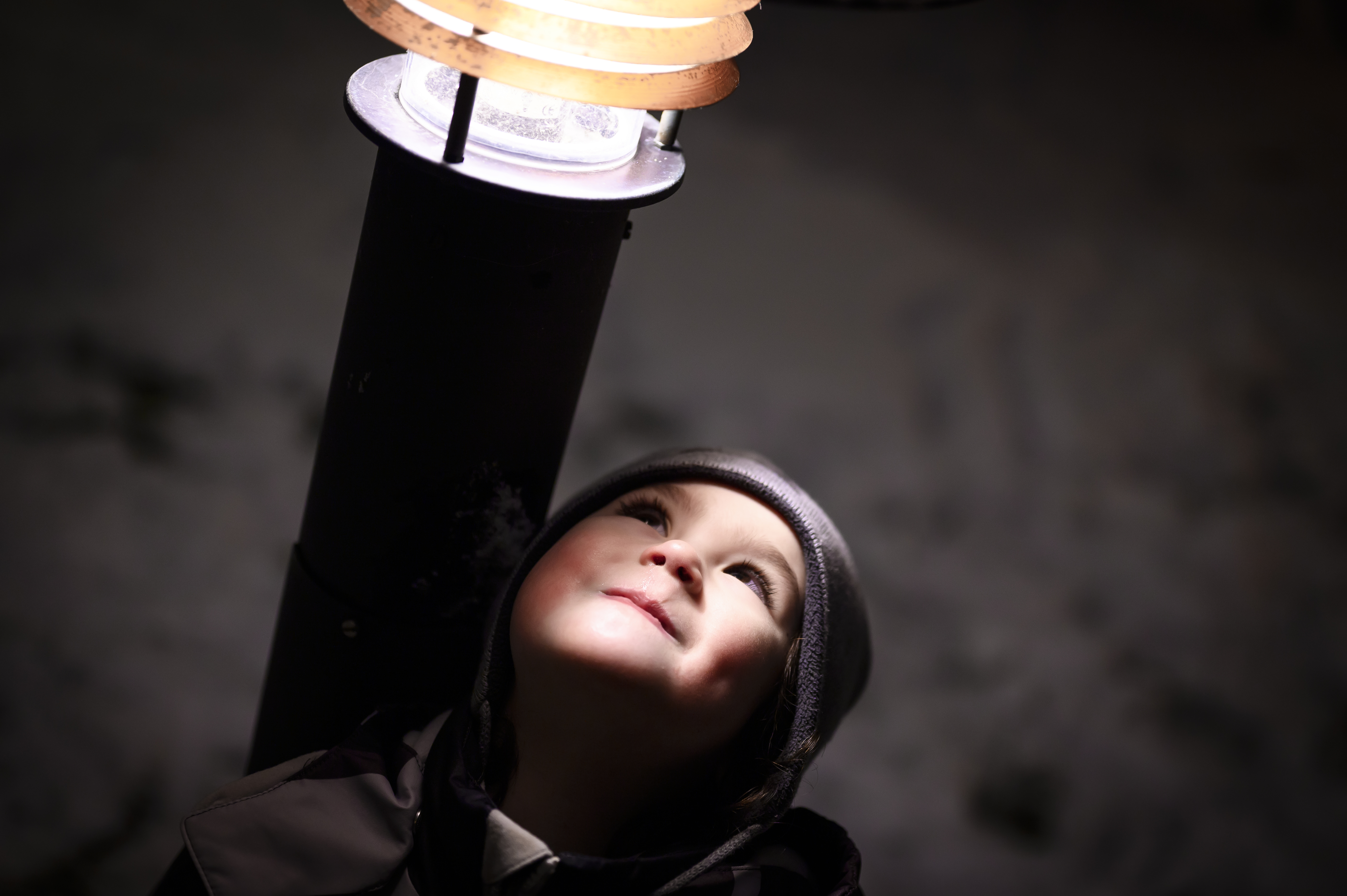 Ett barn står lutat mot en lyktstolpe med ansiktet vänt mot ljuset.