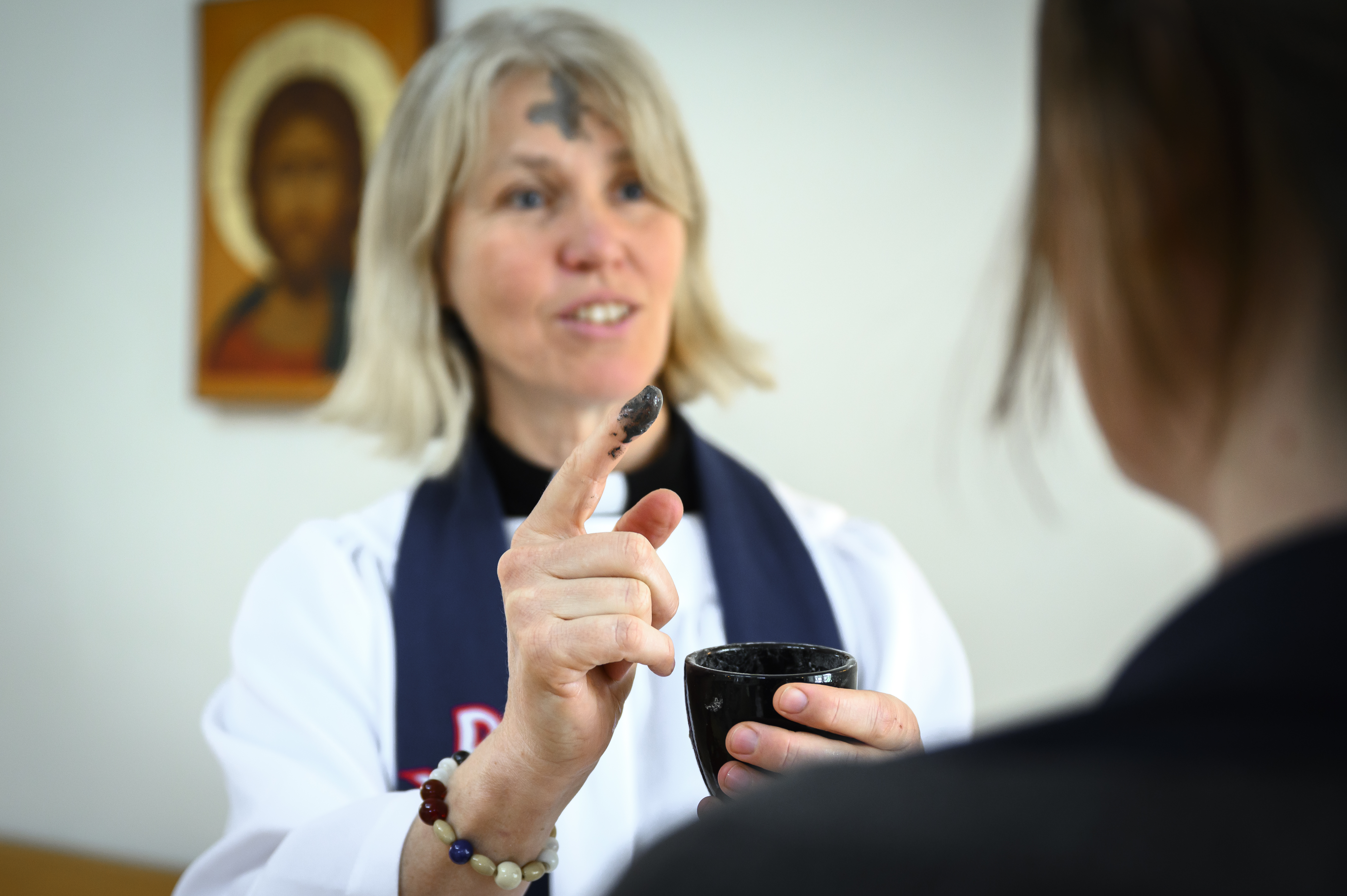 Kvinnlig präst med askkors i pannan har doppat fingret i askan för att göra ett likadant kors på personen framför henne.