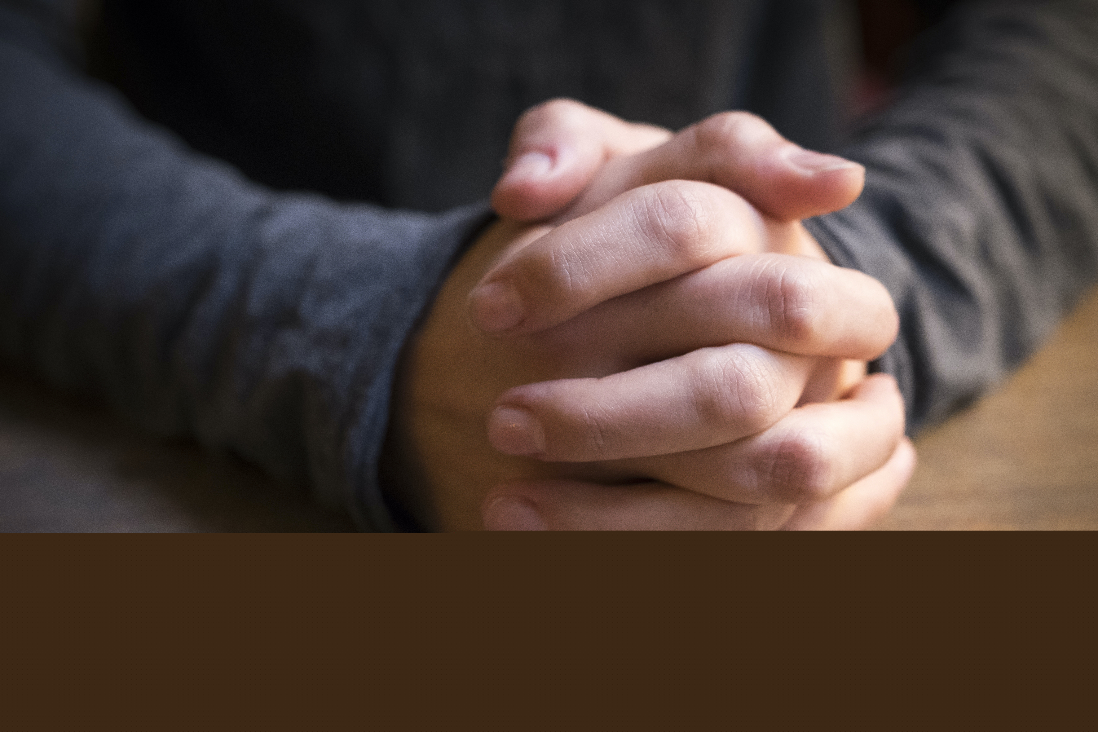 Någons knäppta händer vilar på ett bord.