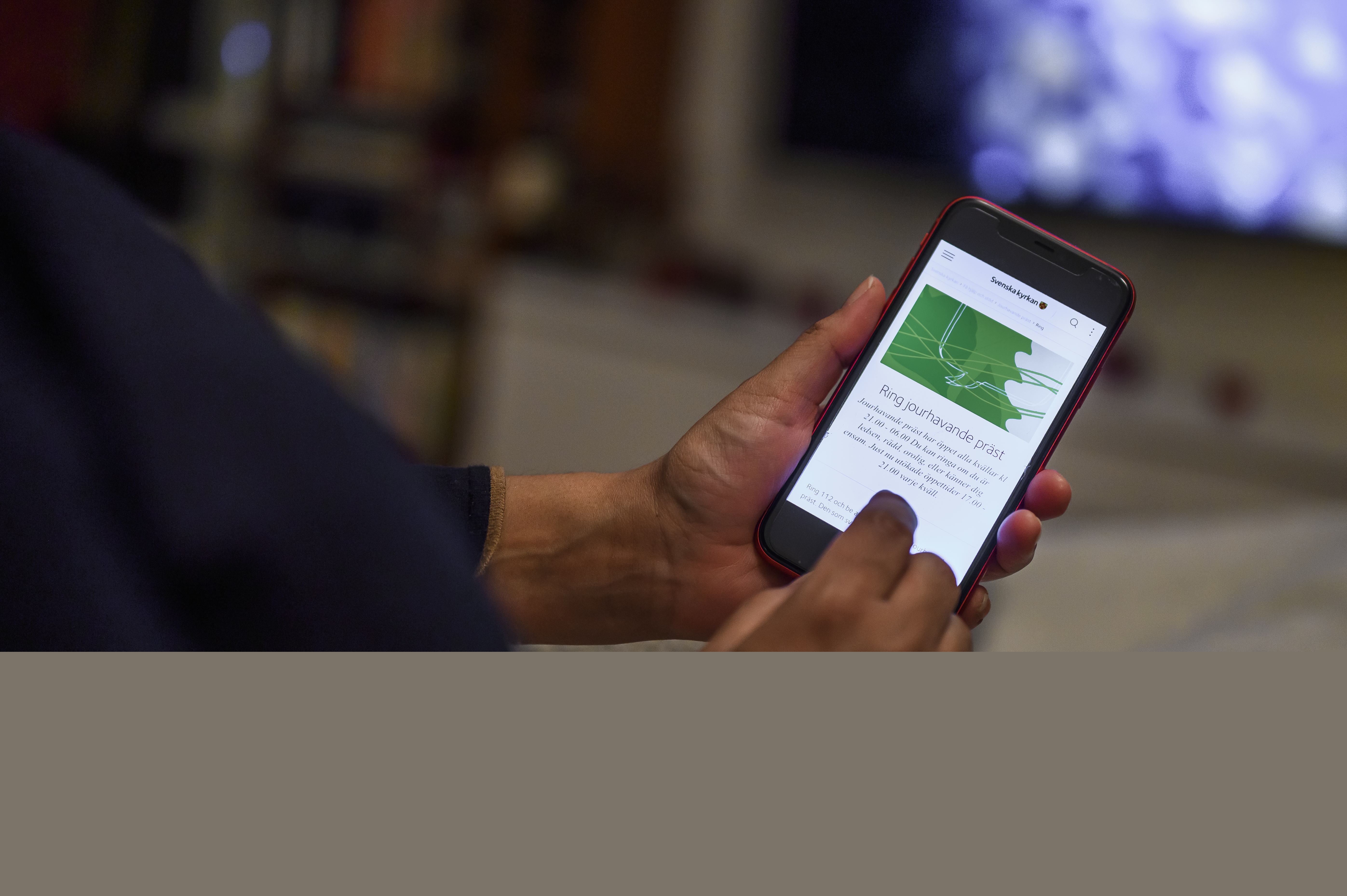 En person har sin mobiltelefon i händerna. Skärmen visar Svenska kyrkans information om jourhavande präster.