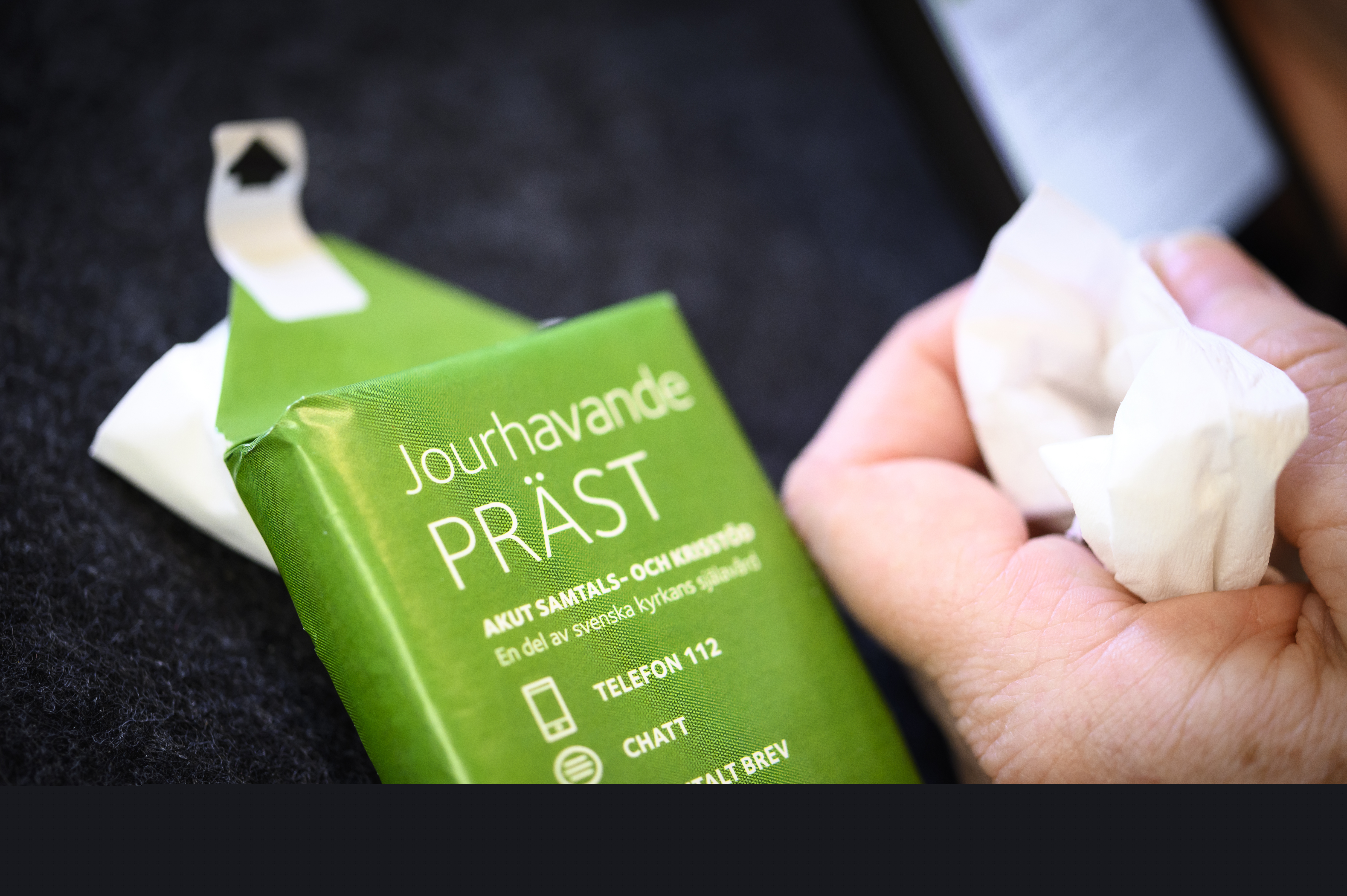 Någon håller en näsduk i handen. En förpackning med visitkort till jourhavande präst ligger bredvid.