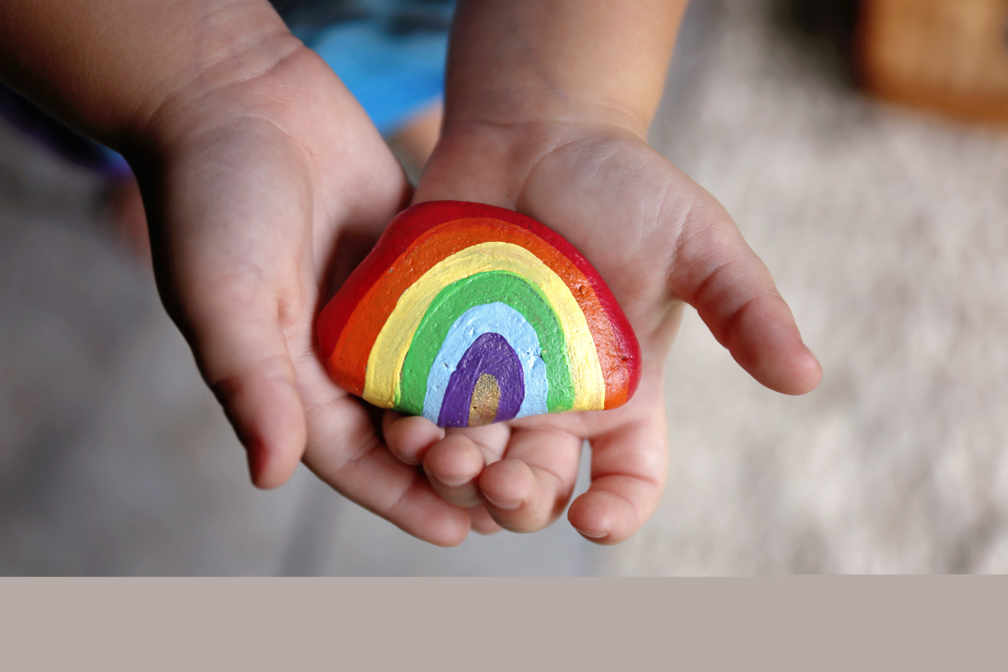 Ett barn håller upp en sten målad som en regnbåge.