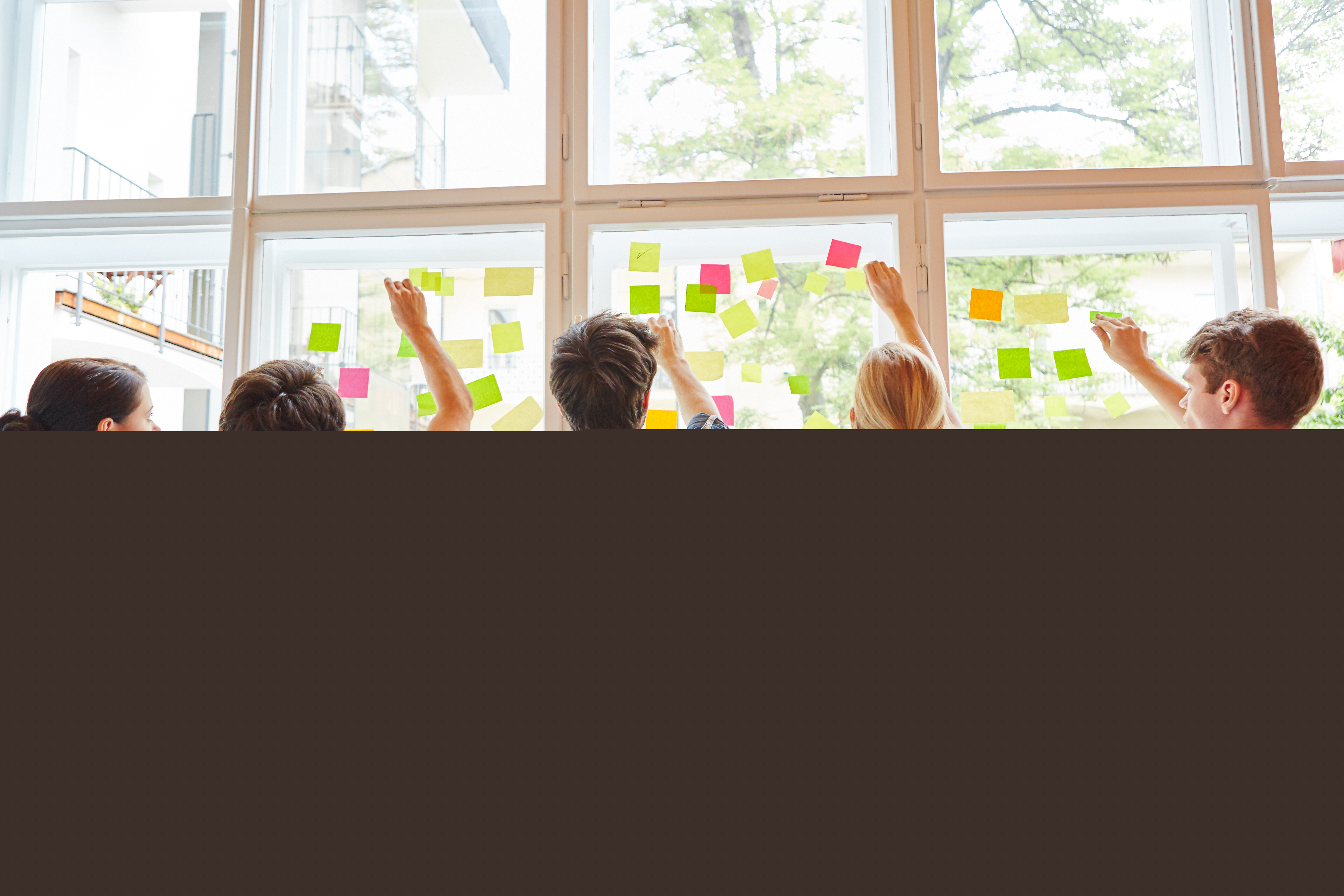 Några ungdomar sätter upp en massa olikfärgade post it-lappar på ett stort fönster.