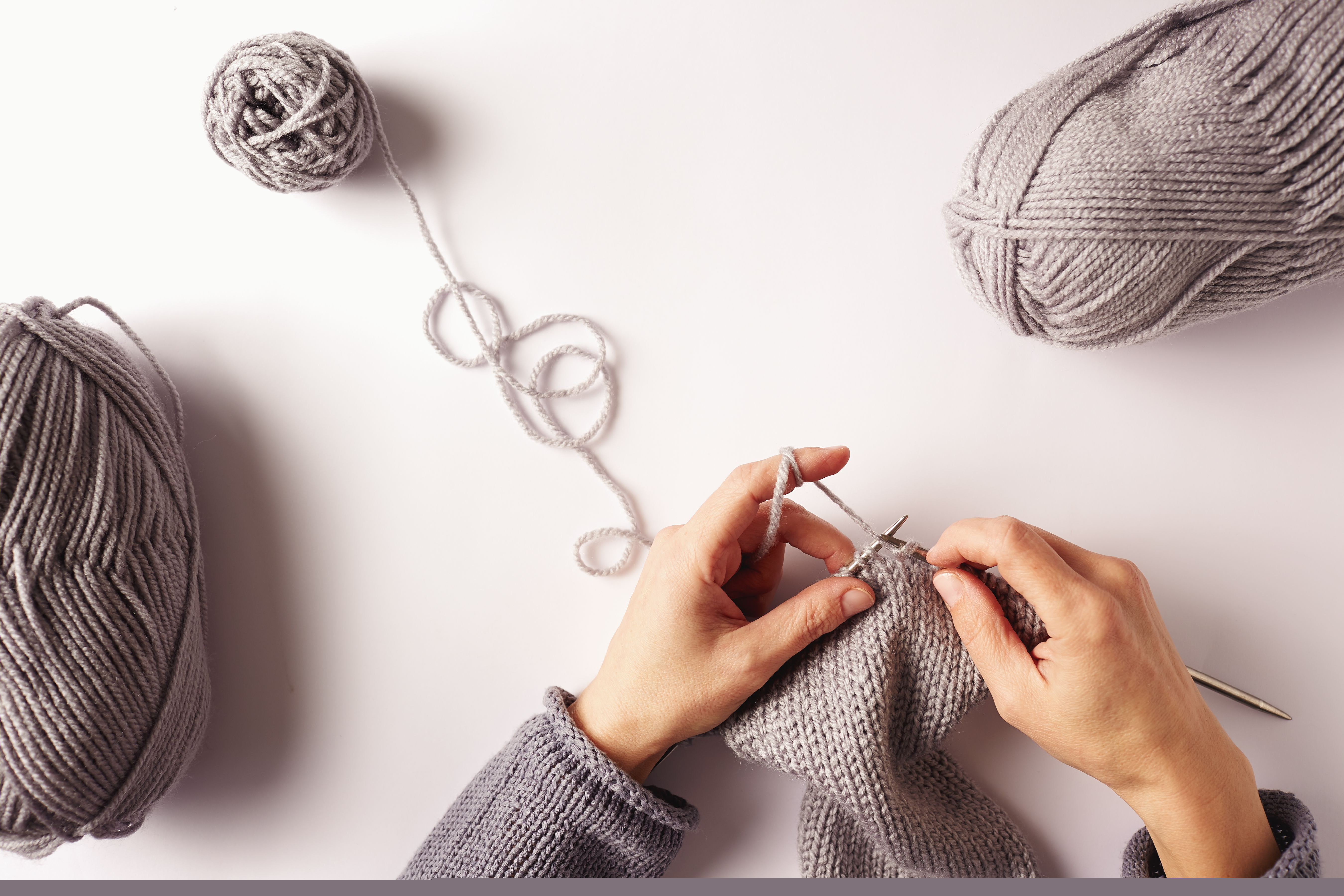 Närbild på två händer som stickar med grått garn.
