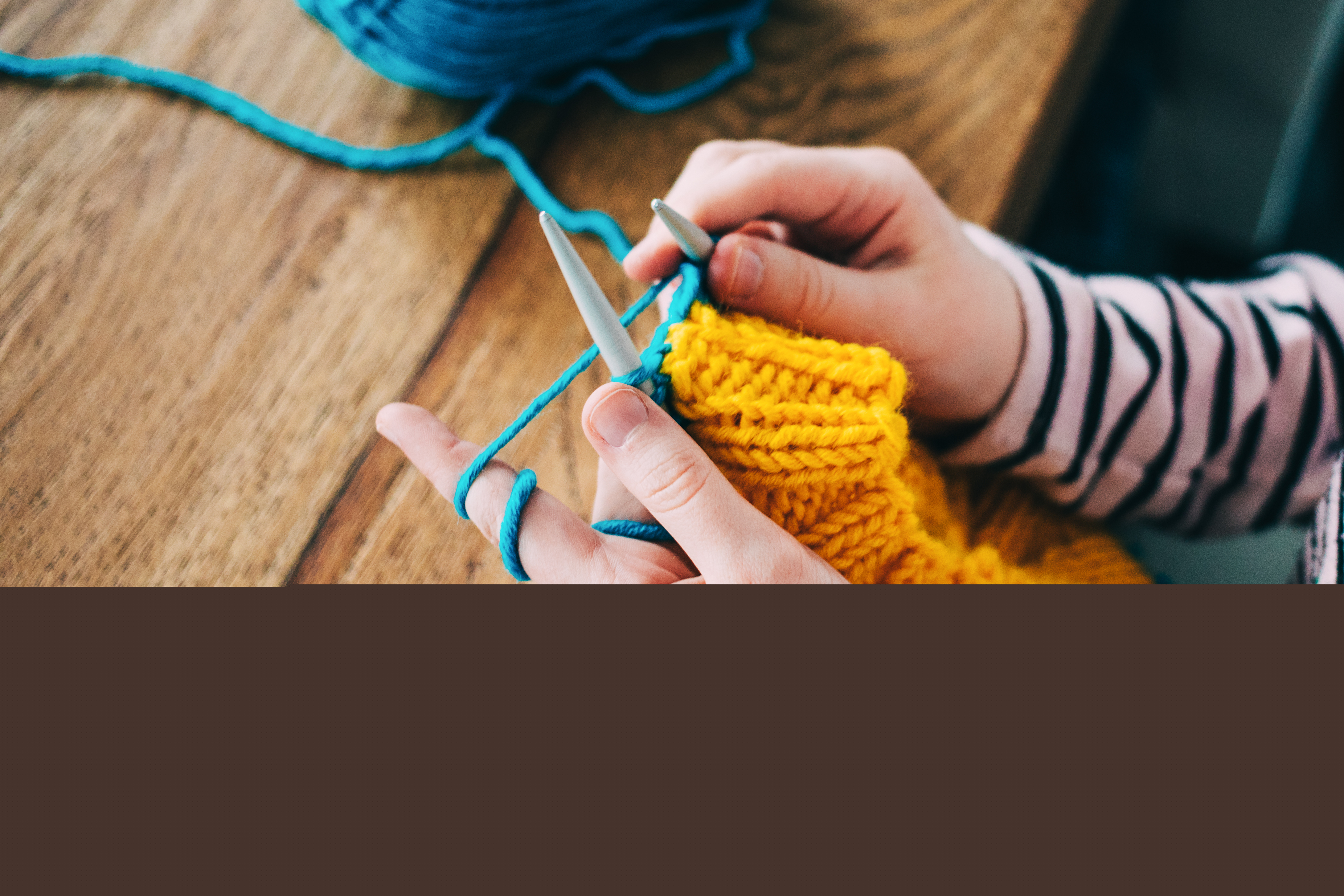 Närbild på en person som stickar med gult och blått garn.