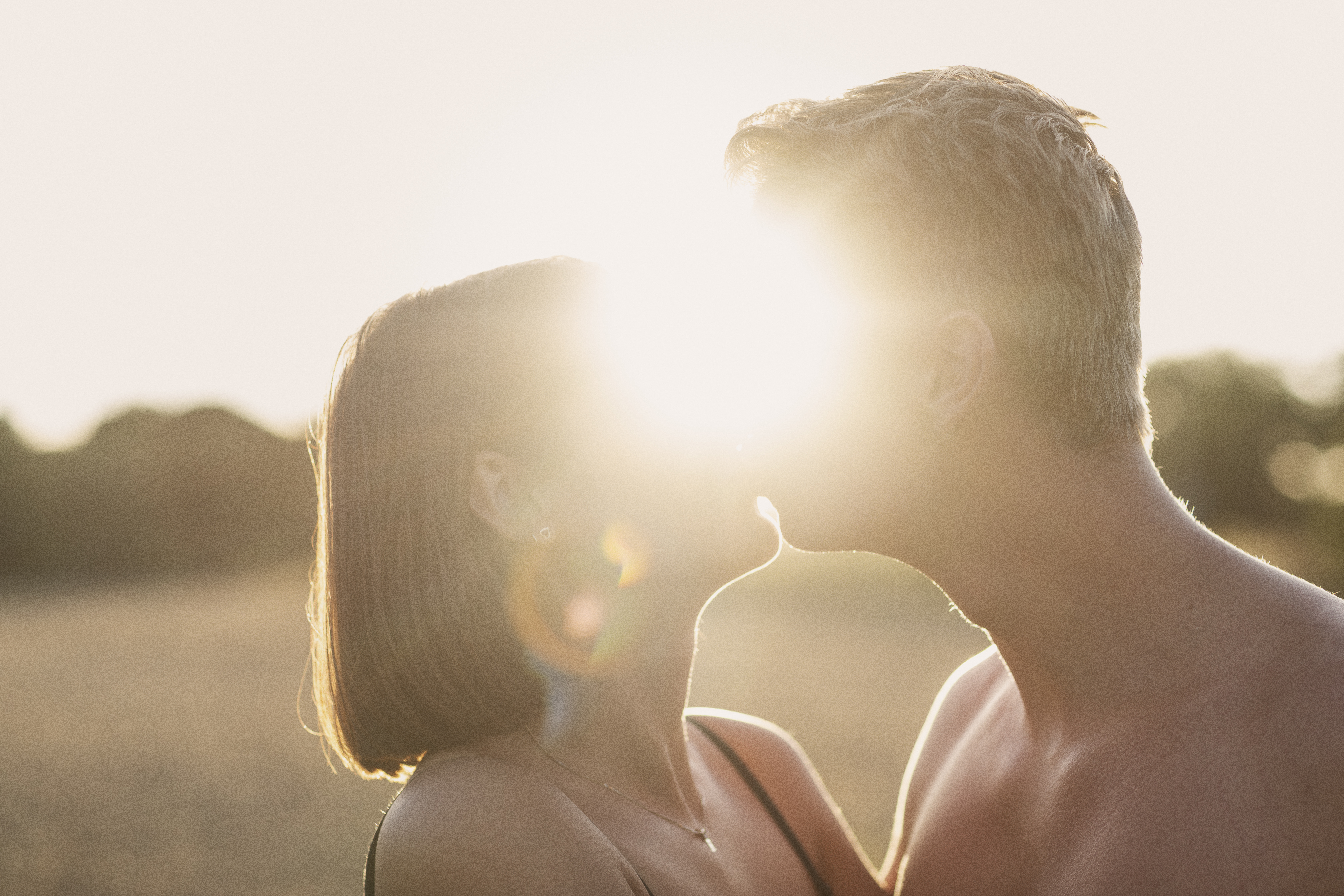 En man och en kvinna kysser varandra. Solen lyser igenom mellan deras ansikten.
