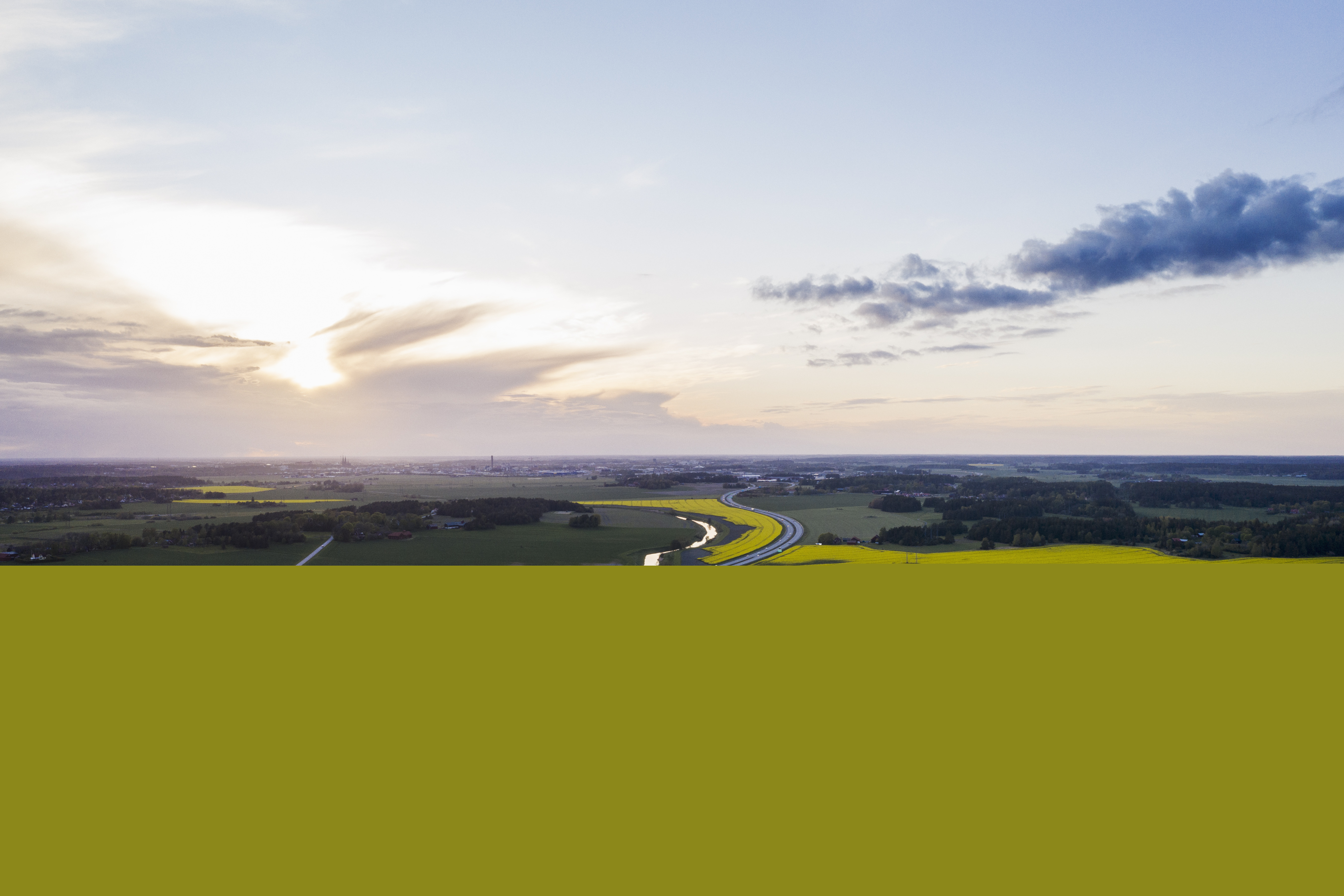 Flygfoto över en bilväg och en å genom ett fält.