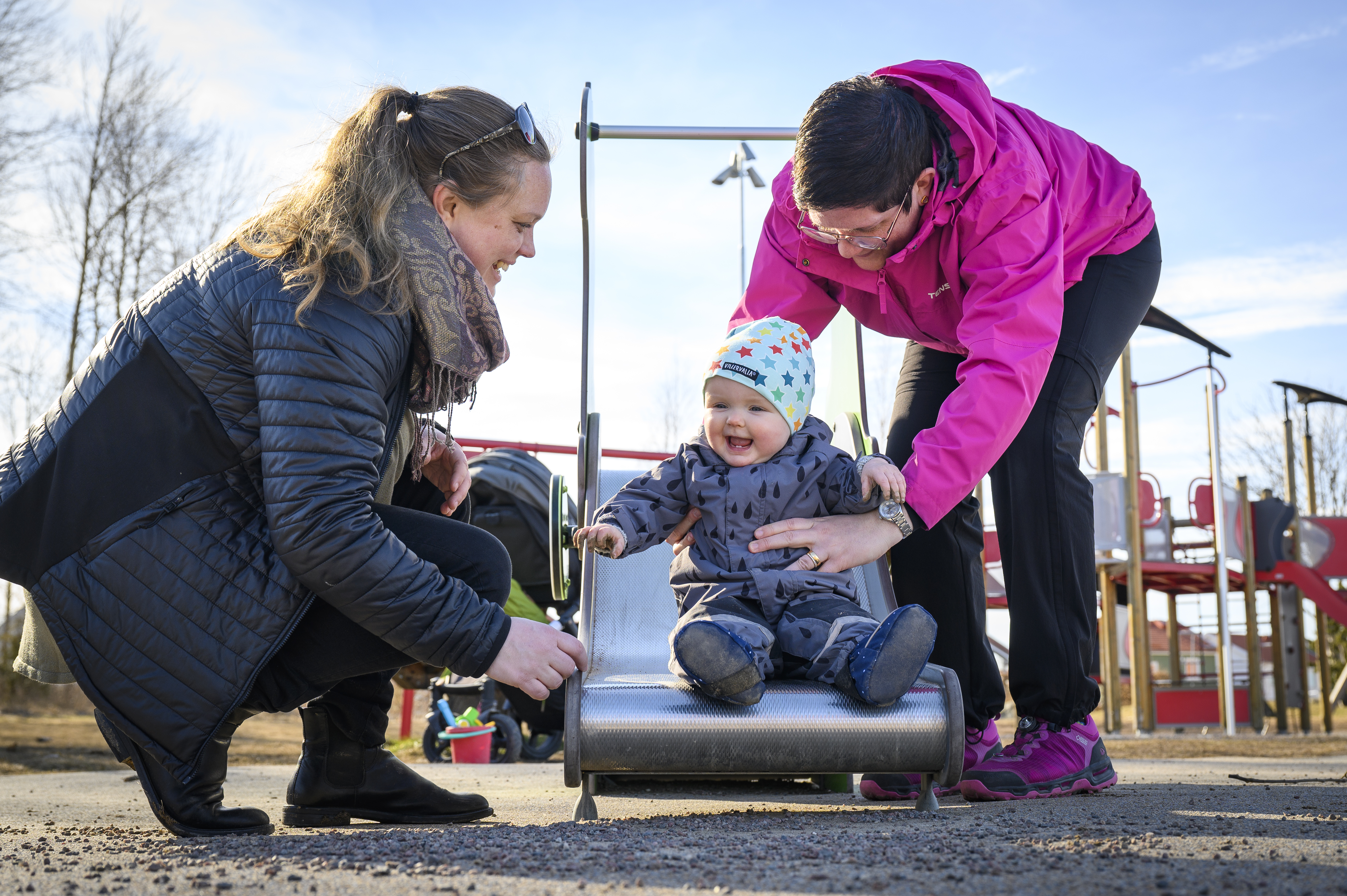 Två föräldrar hjälper sin bebis nedför rutschbanan.