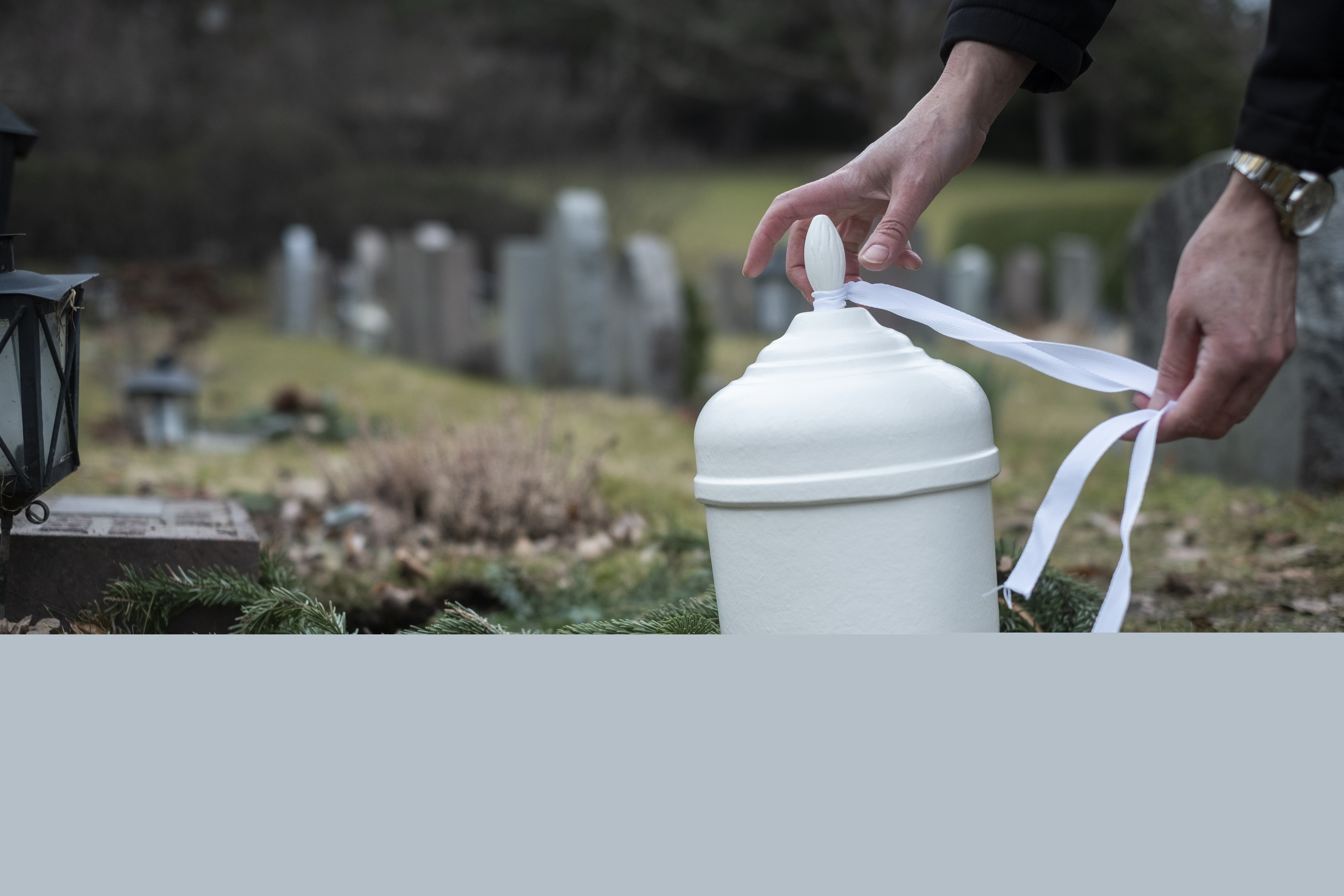 Någon knyter ett vitt band runt en vit urna på en kyrkogård.