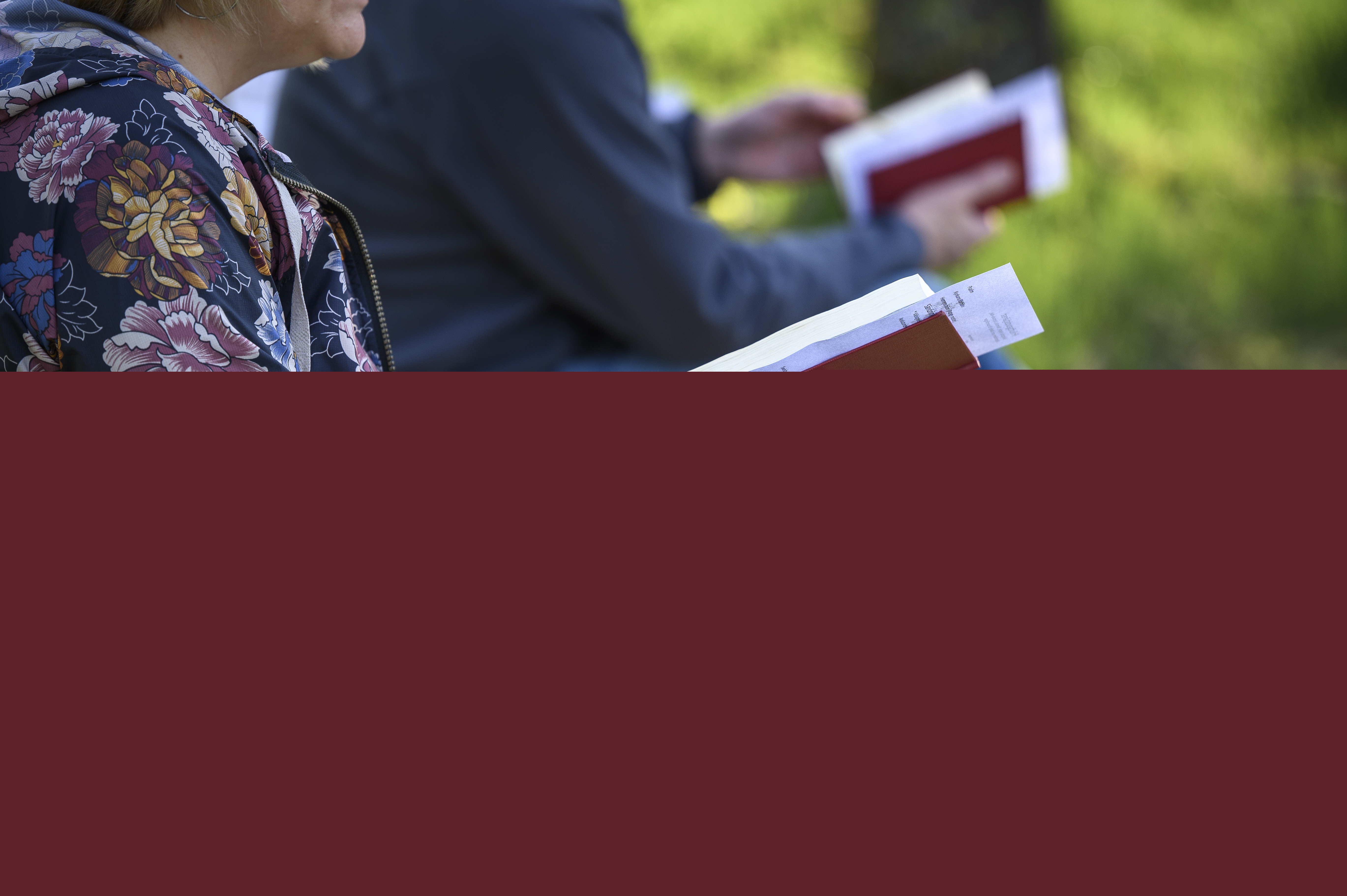 Två personer sitter bredvid varandra utomhus med varsin psalmbok.