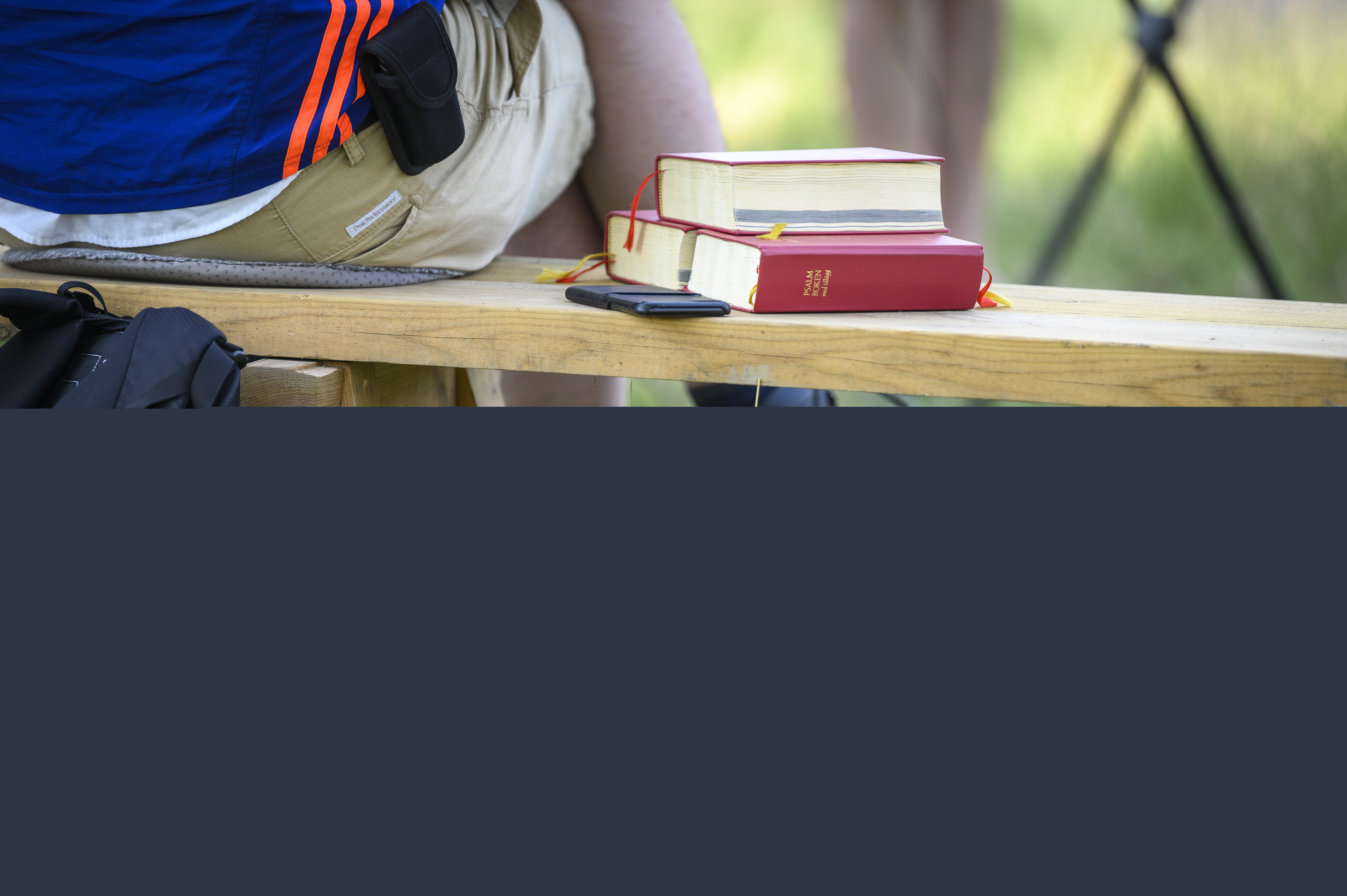 Någon sitter på en bänk utomhus. Bredvid ligger några psalmböcker.