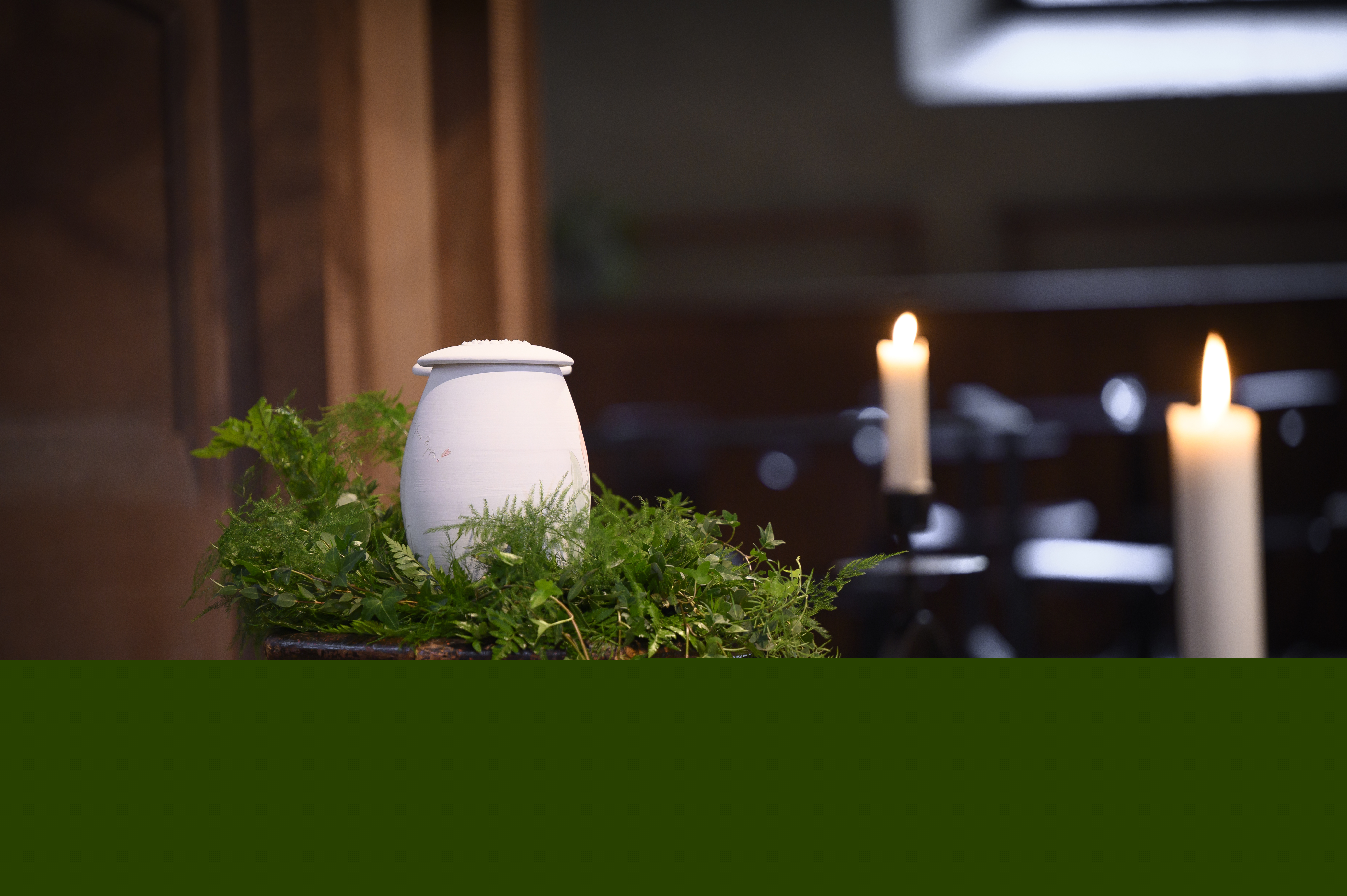 En urna står uppställd bland ormbunksblad i kyrkan.
