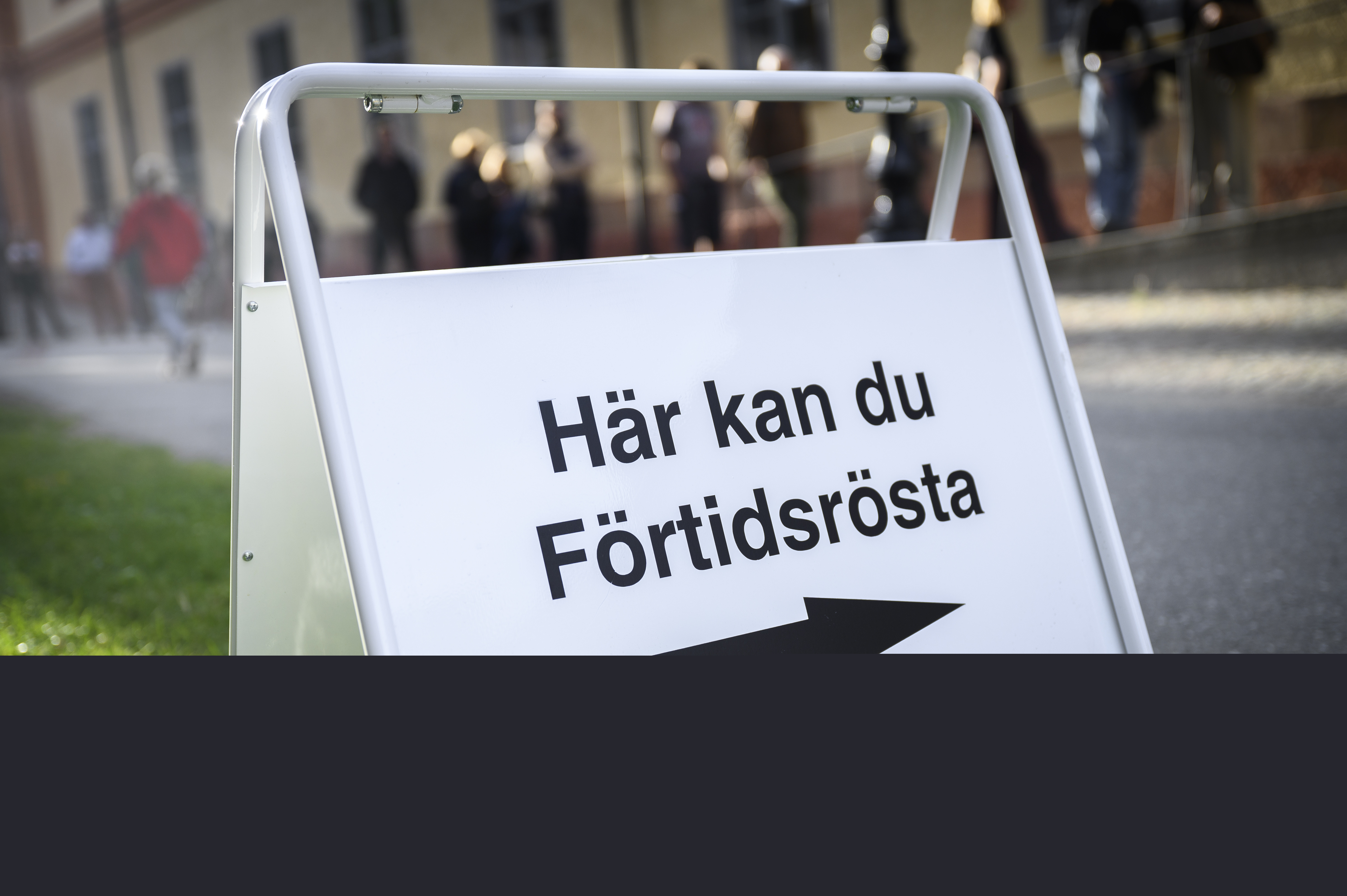 En skylt med texten Här kan du Förtidsrösta. Köande människor i bakgrunden.