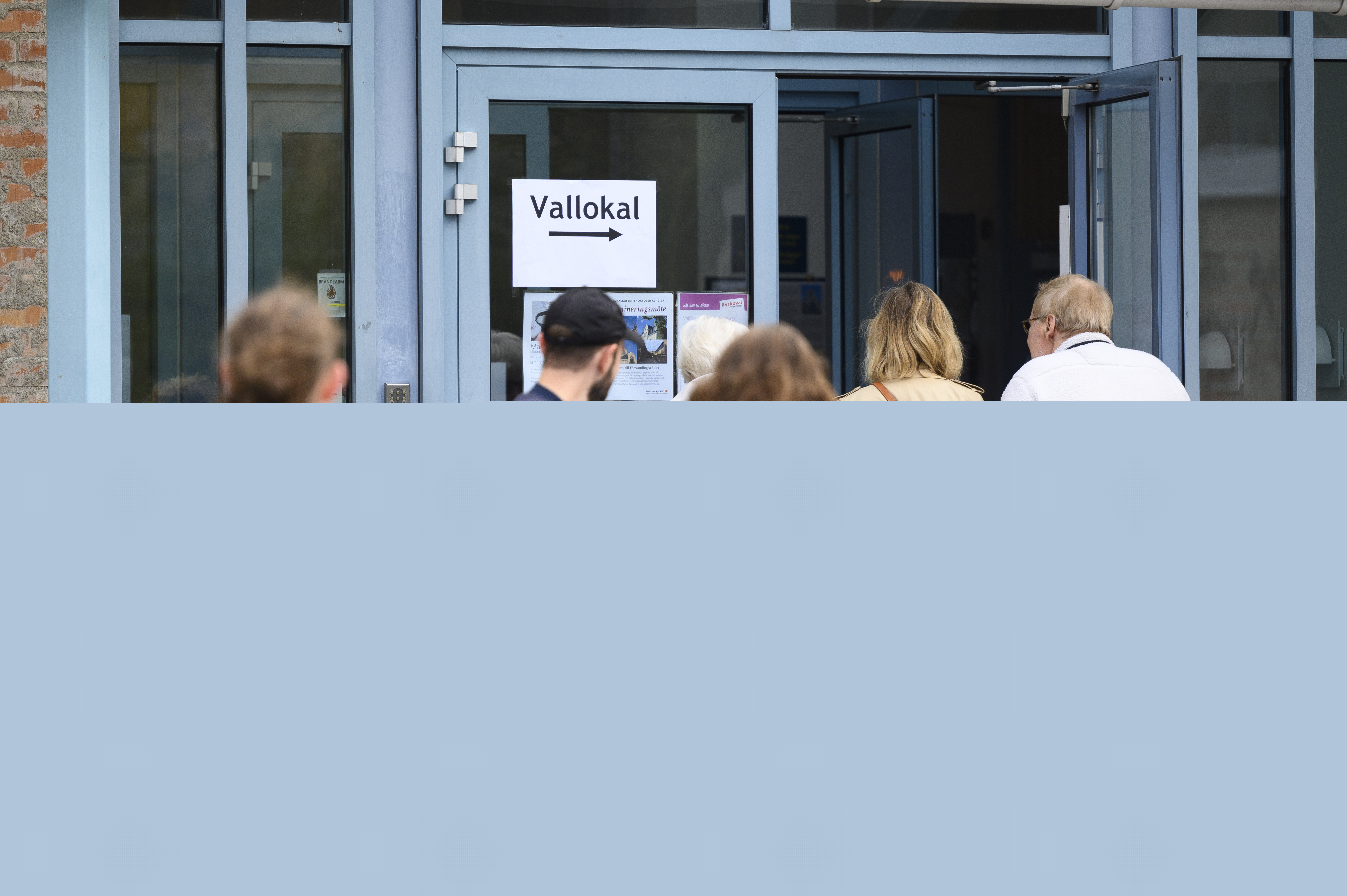 Människor som köar utanför en kyrka. Vid den öppna dörren sitter en lapp med texten Vallokal.