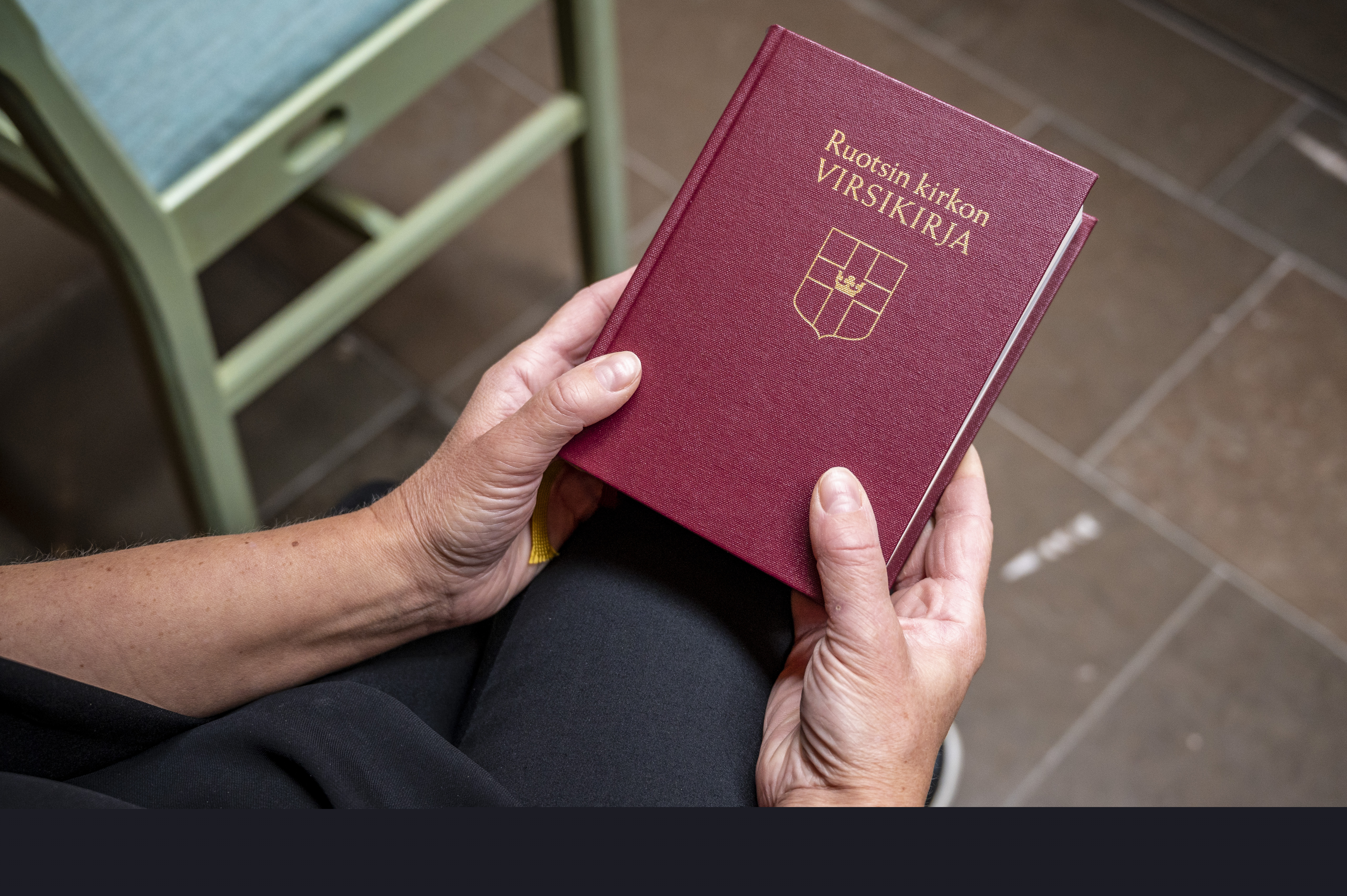 Någon sitter i ett kapell och håller en finsk psalmbok i händerna.