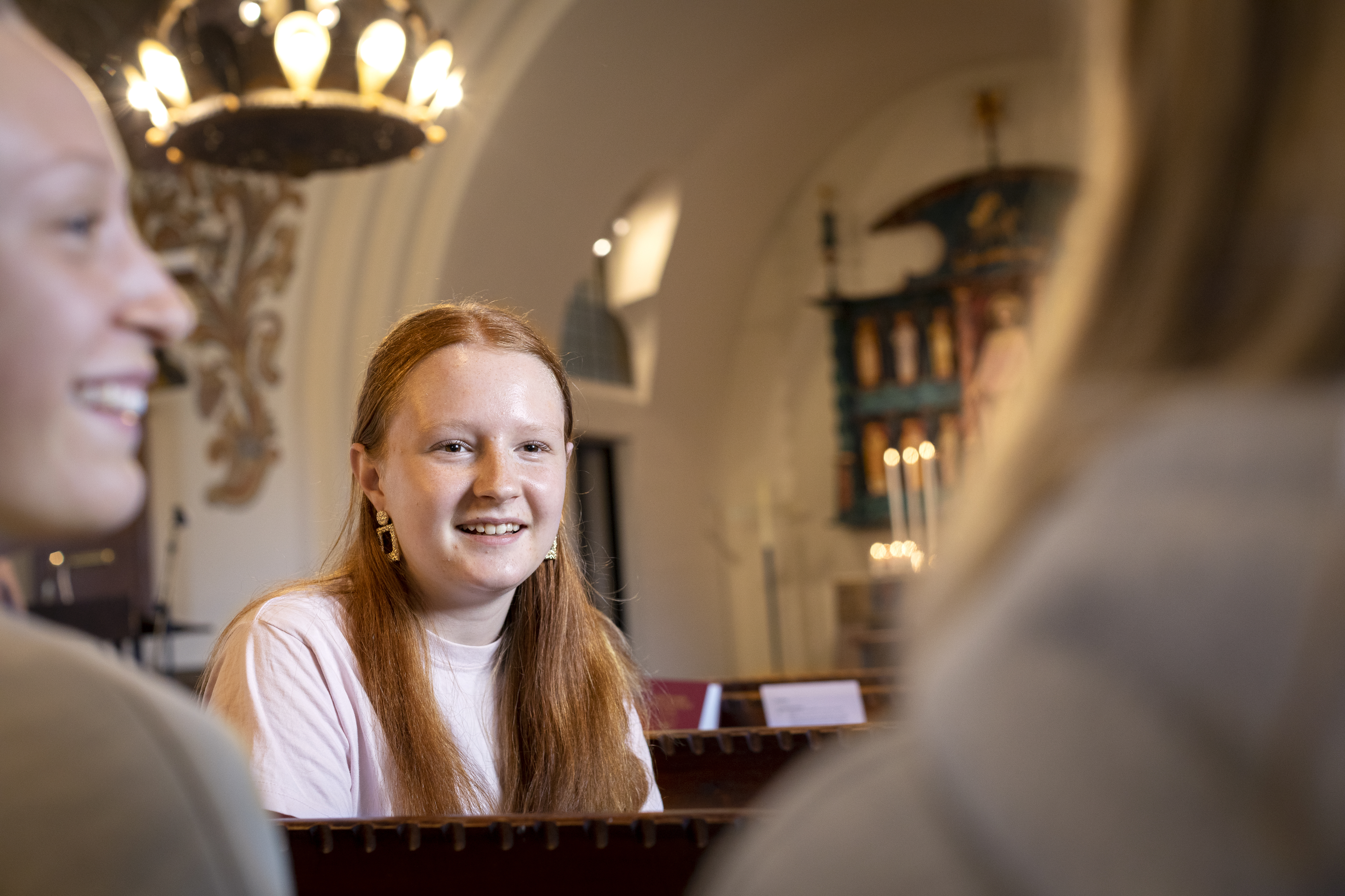En rödhårig tonårstjej sitter i en kyrkbänk och snackar med några jämnåriga.