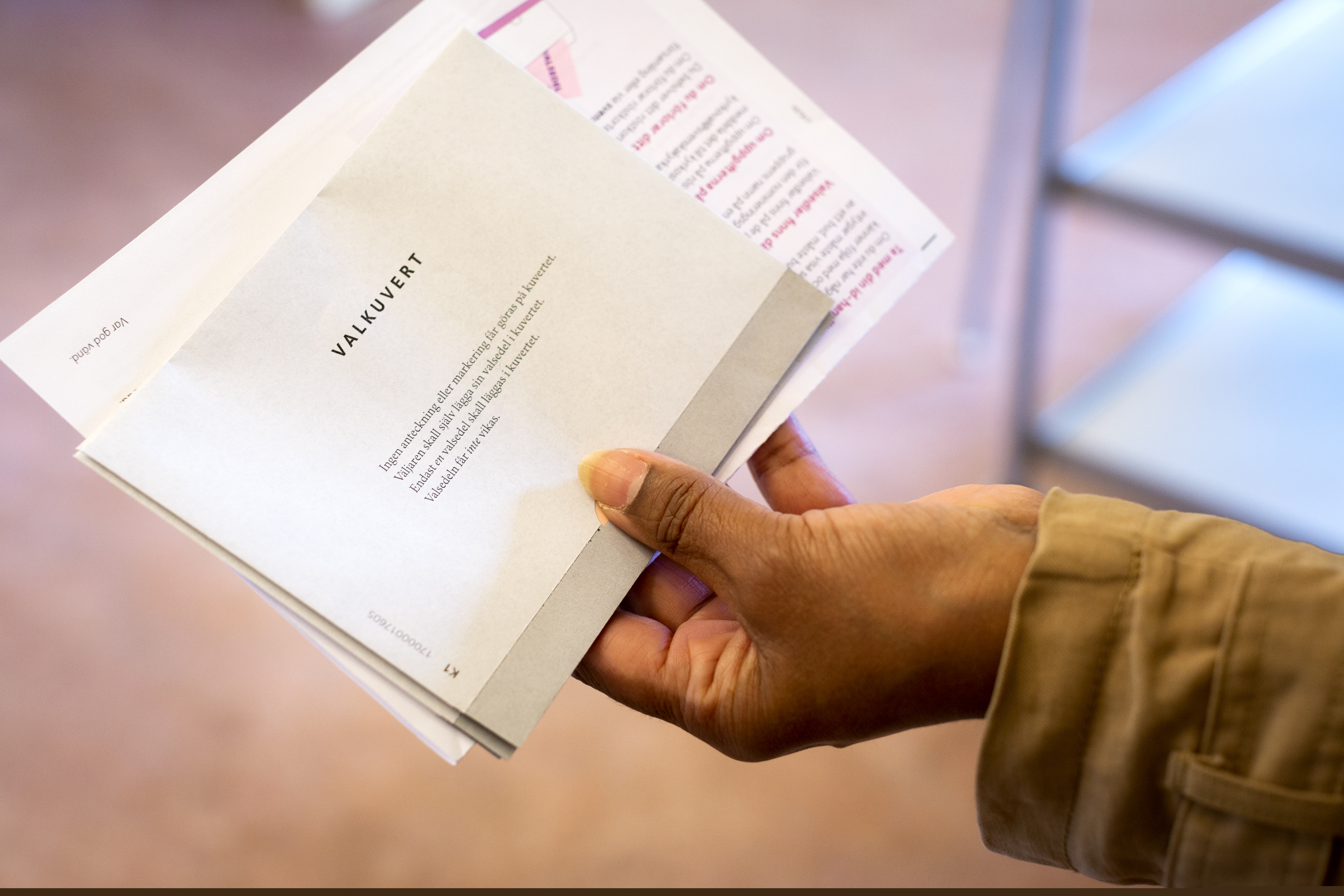 Närbild på en hand som håller ett valkuvert och ett röstkort.