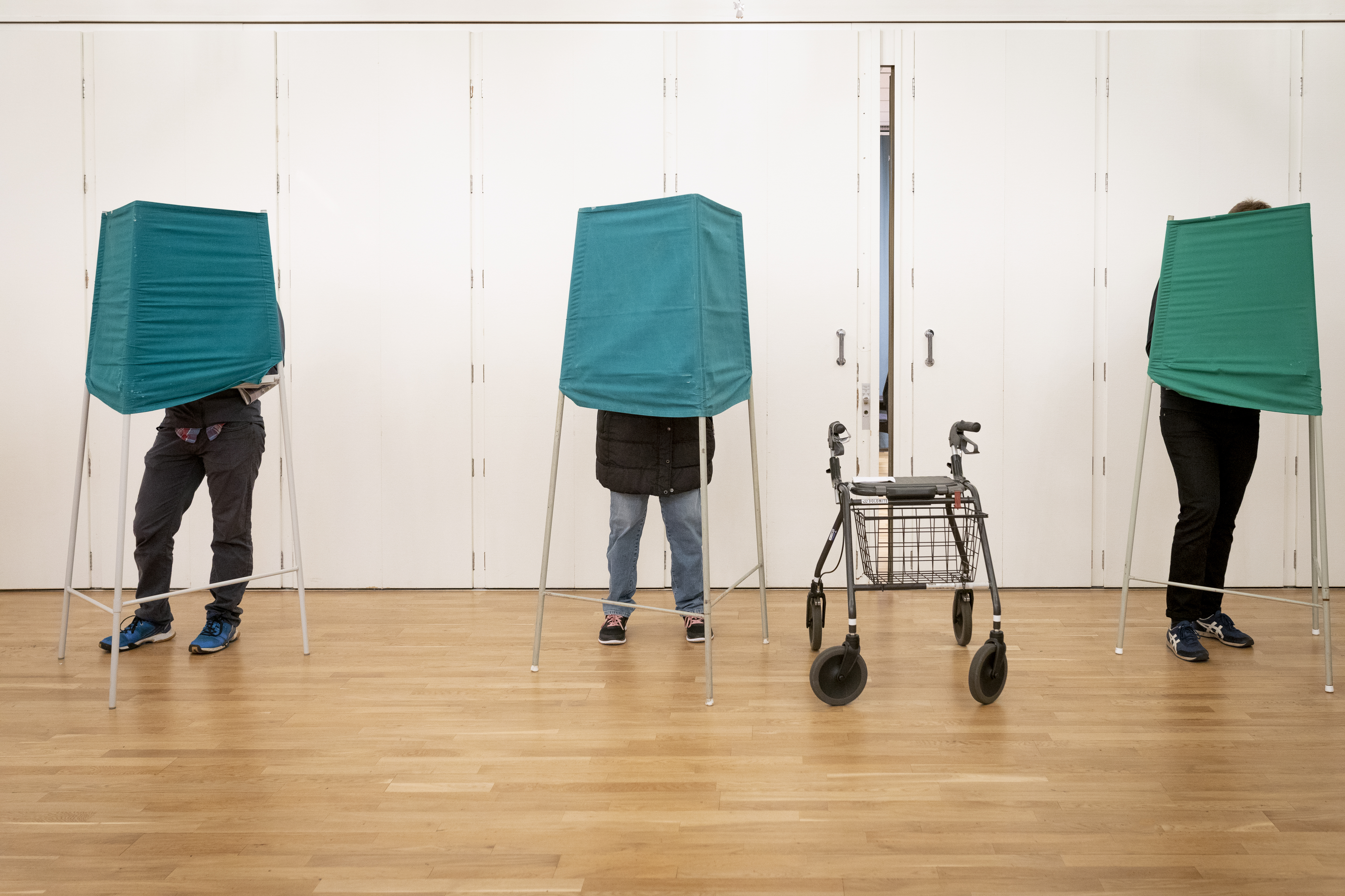 Tre stycken gröna valbås med människor som röstar. En rullator står bredvid.