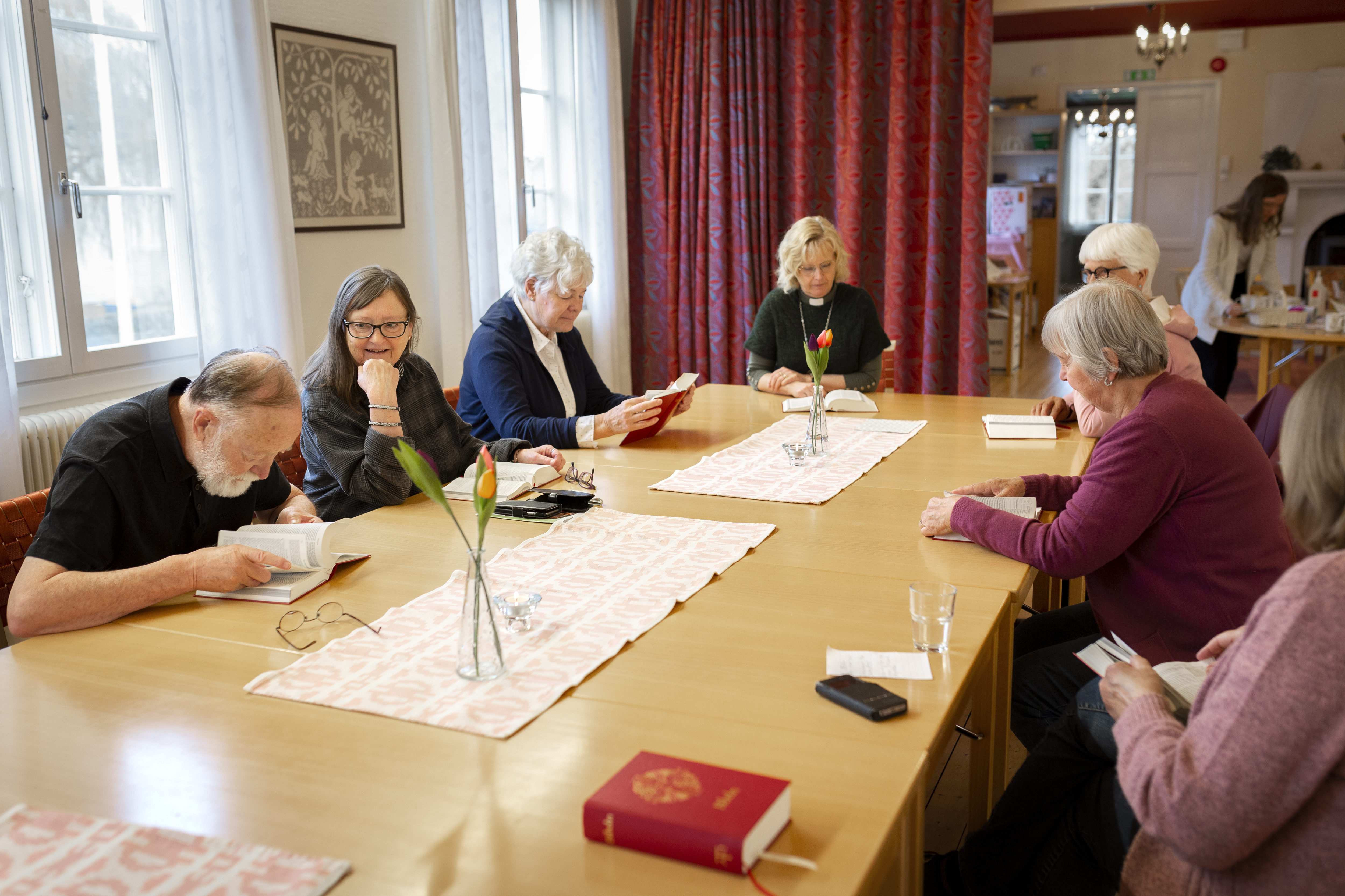 En grupp sitter runt ett mötesbord, alla med var sin bibel framför sig.
