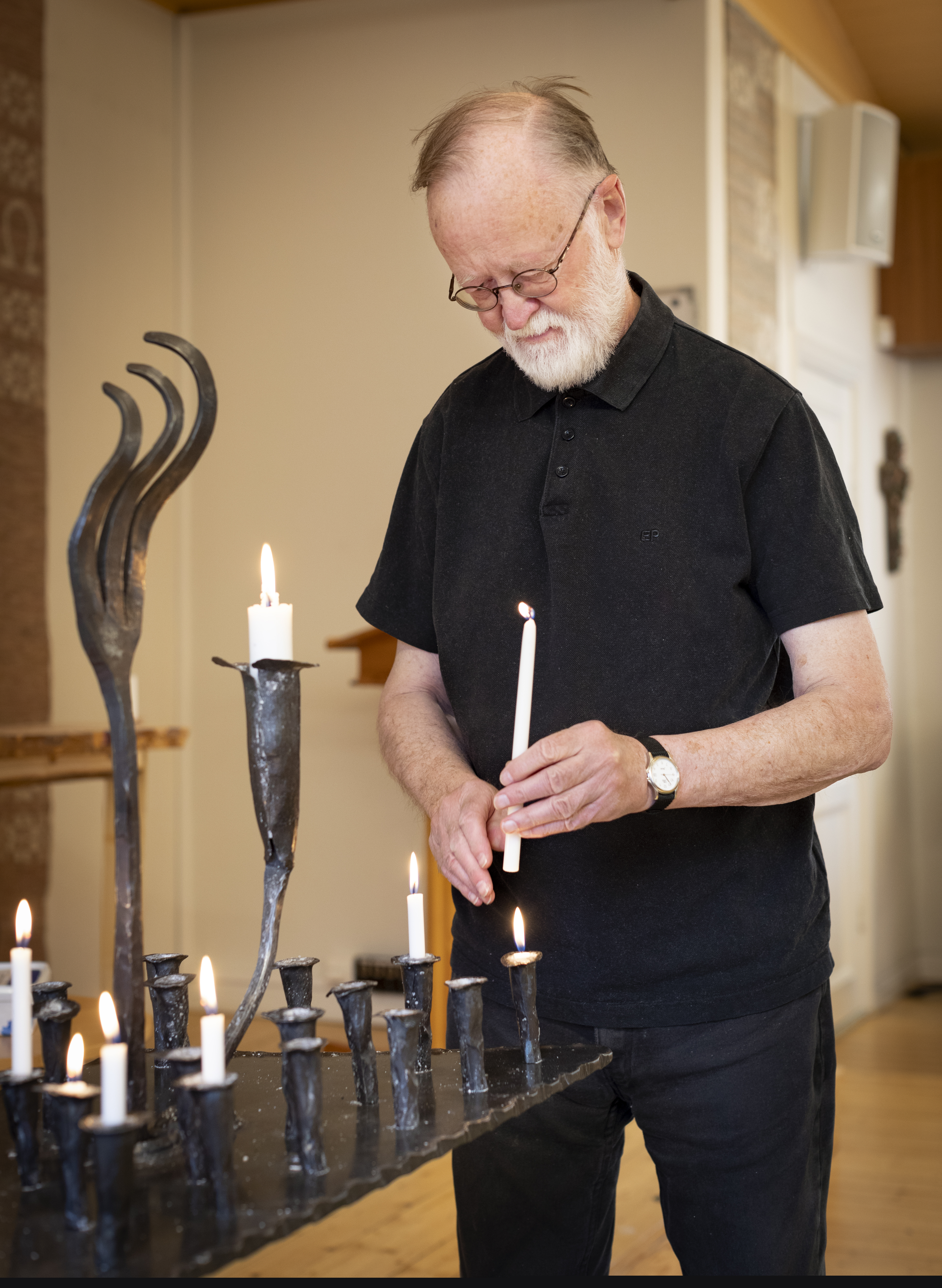 En svartklädd man sätter ett tänt ljus i en svart 
smidesljusstake.