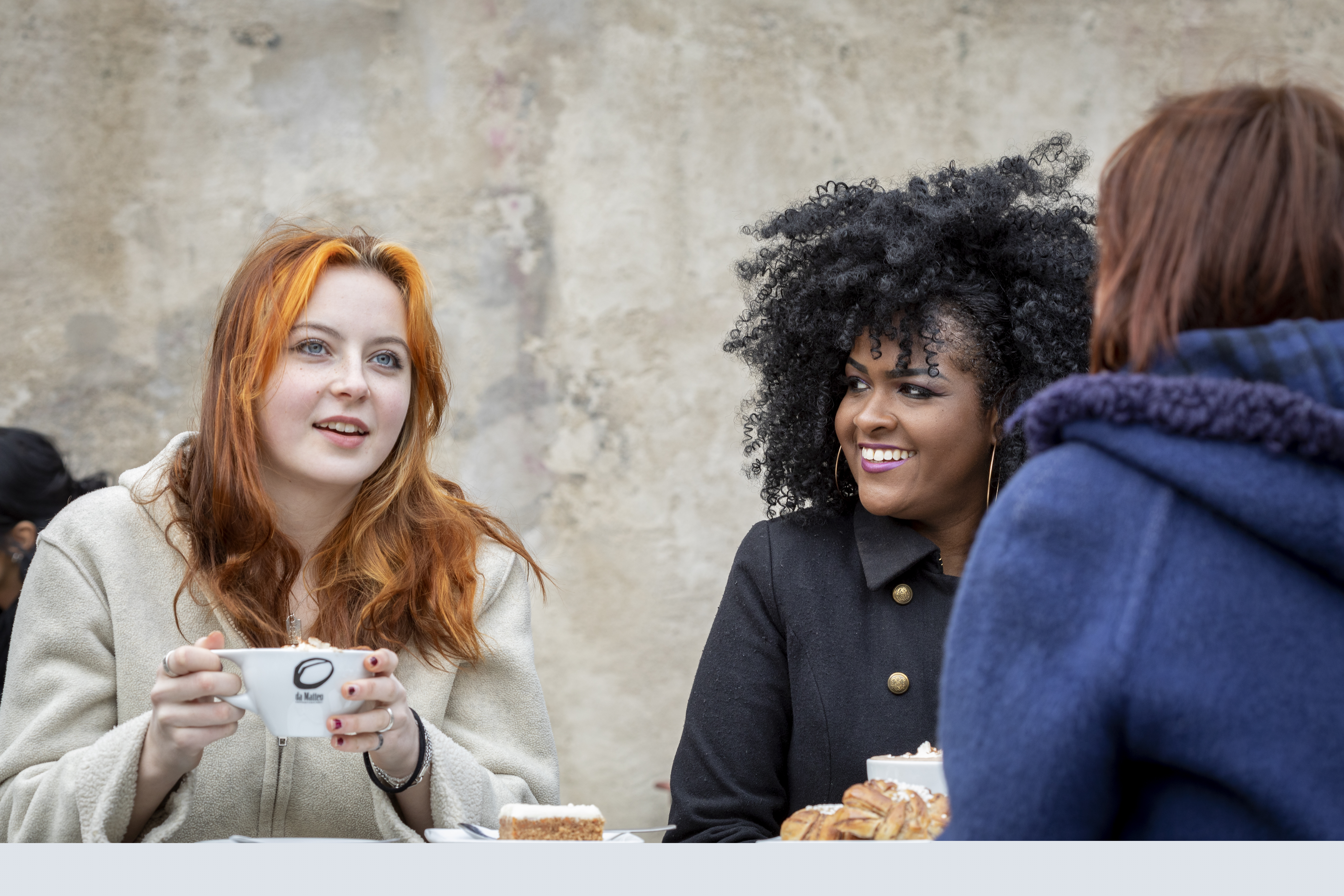 Några unga kvinnor sitter och fikar utomhus.