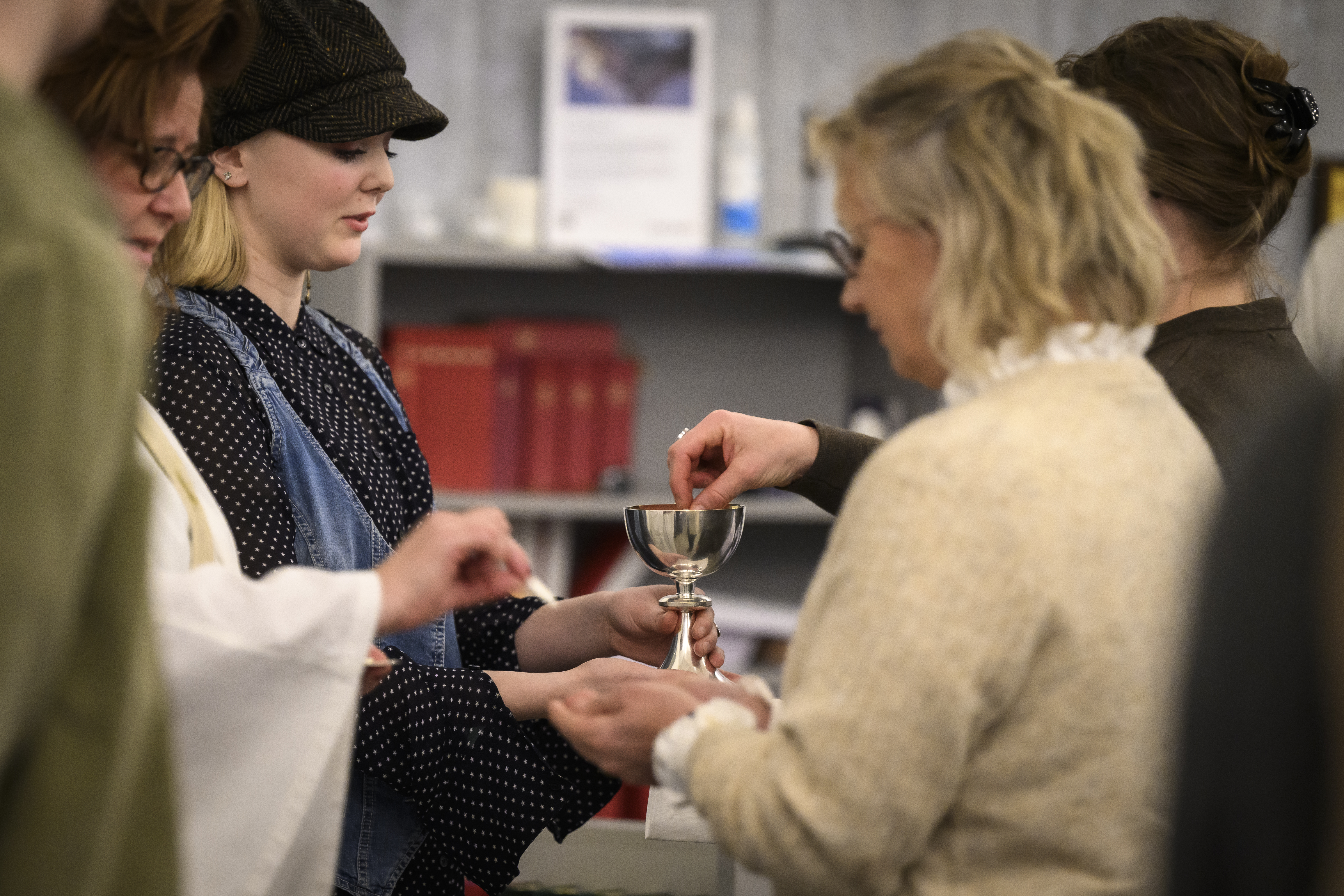 En tjej i manchesterkeps håller fram en nattvardskalk till en kvinna som doppar en oblat däri.