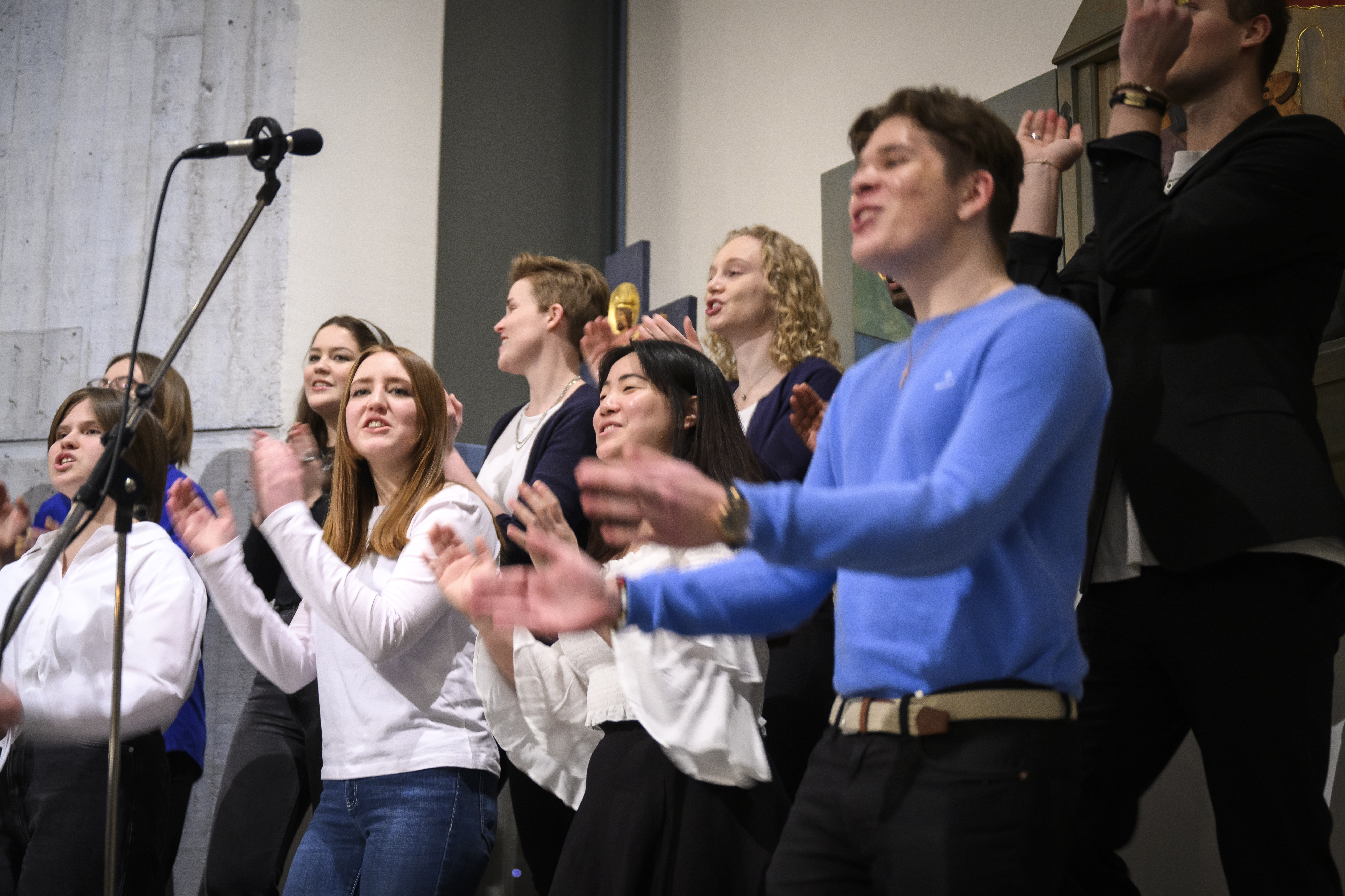 En blandad ungdomskör sjunger och klappar händer inomhus.