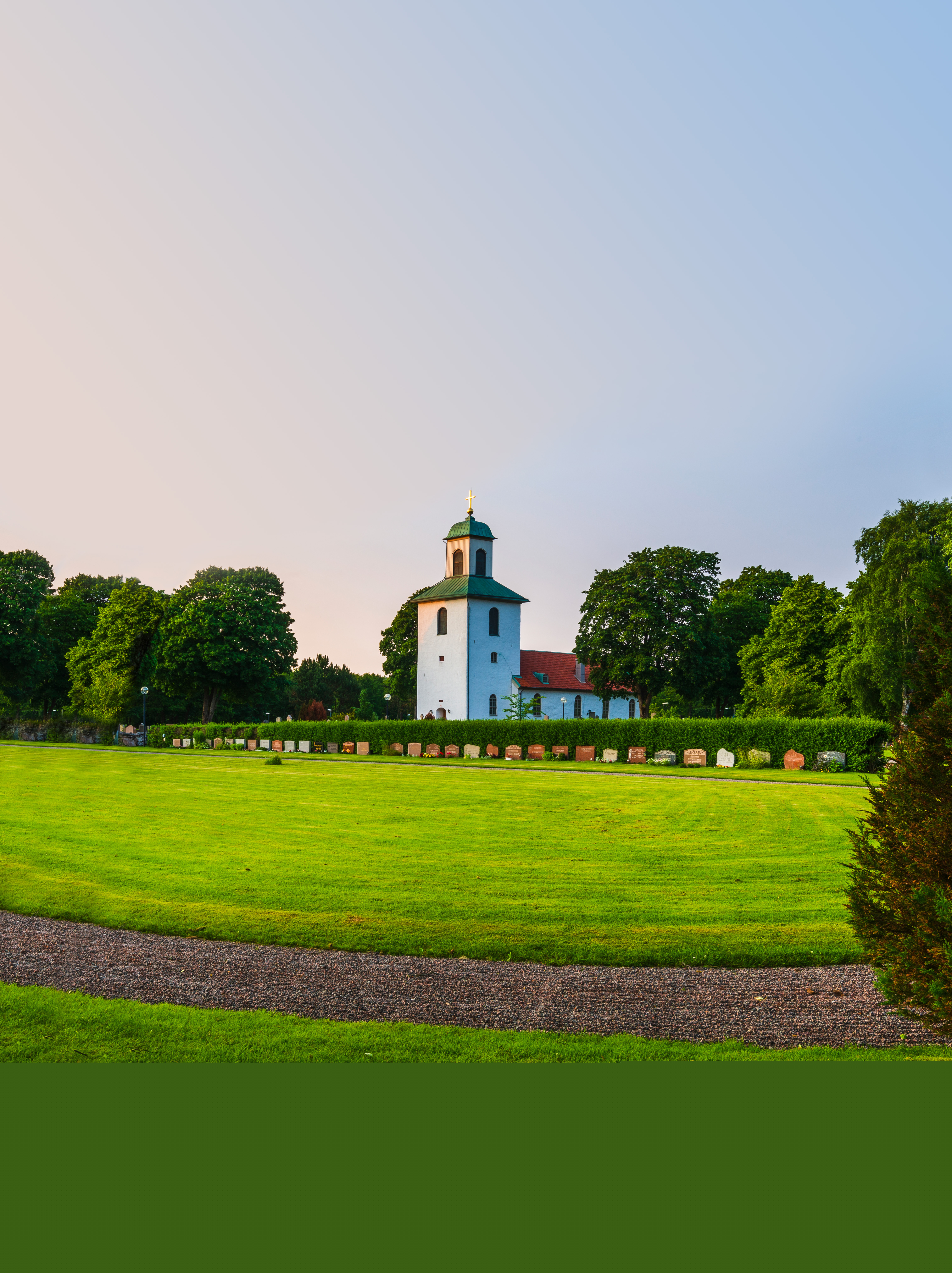 En vit landsbygdskyrka bland lummiga träd.