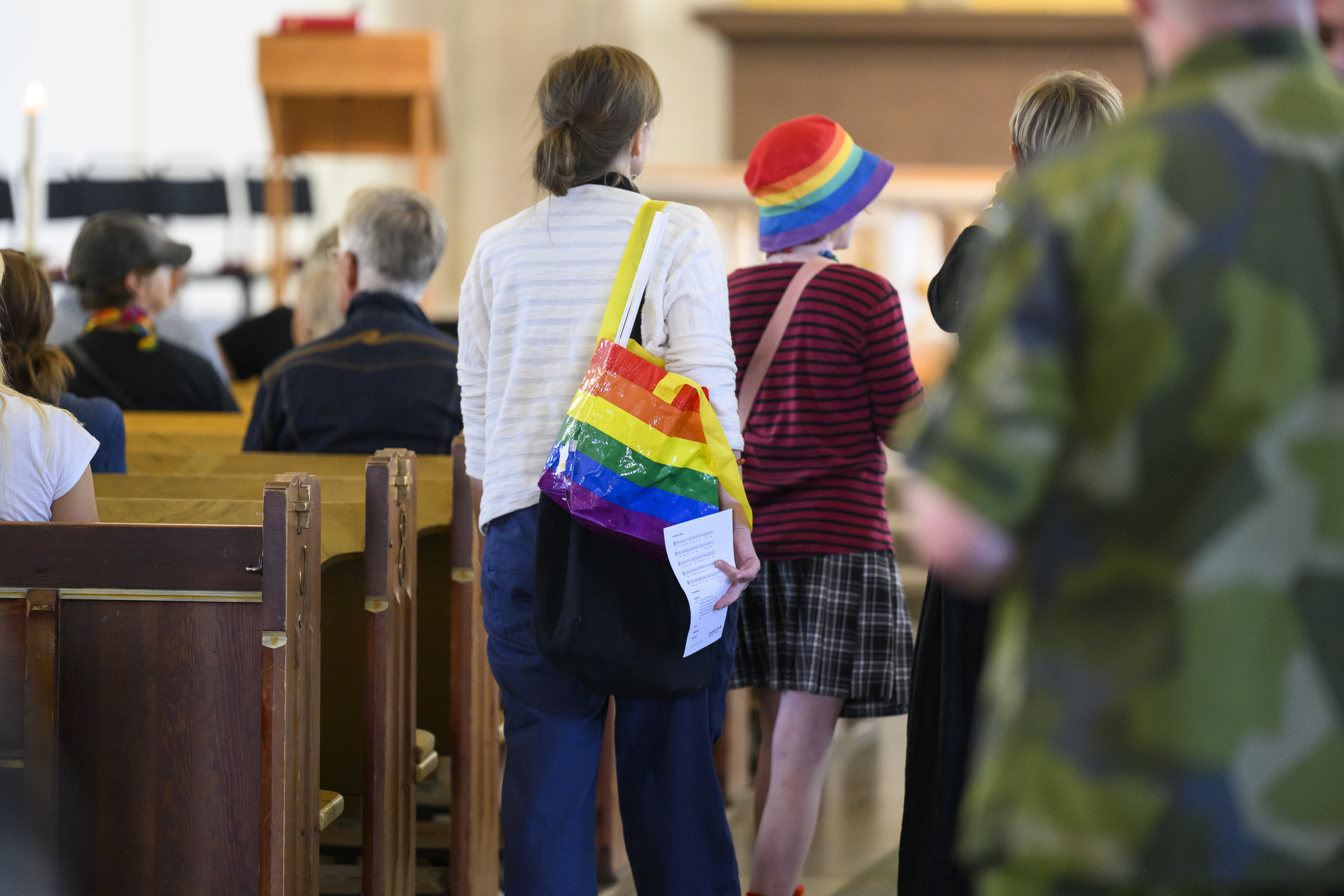 Några personer med regnbågsfärgade accessoarer går i mittgången i en kyrka.