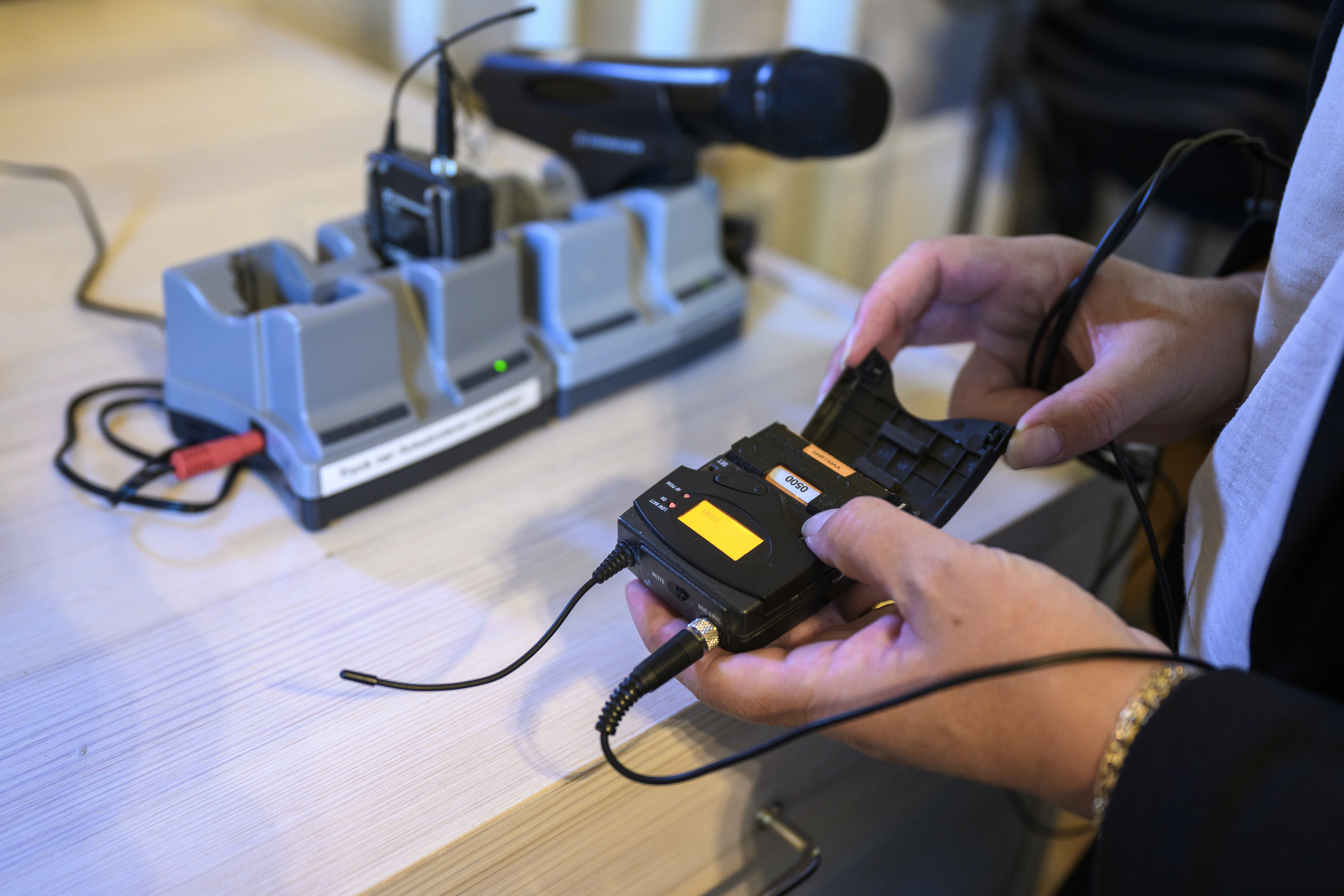 En person håller i en liten trådlös sändare. En mikrofon står och laddar i bakgrunden.