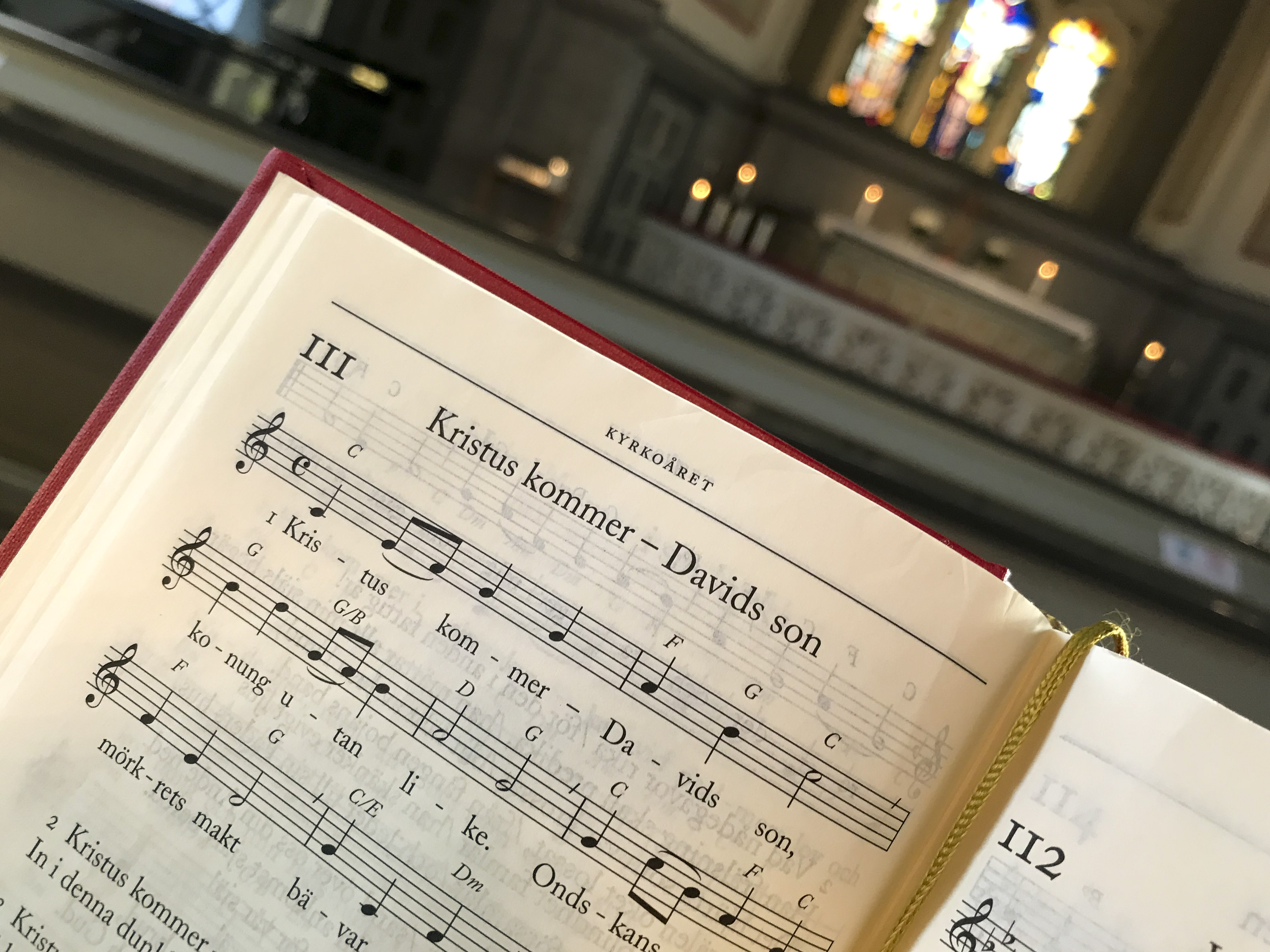 Närbild på en sida ur en psalmbok. Ett altare skymtas i bakgrunden.