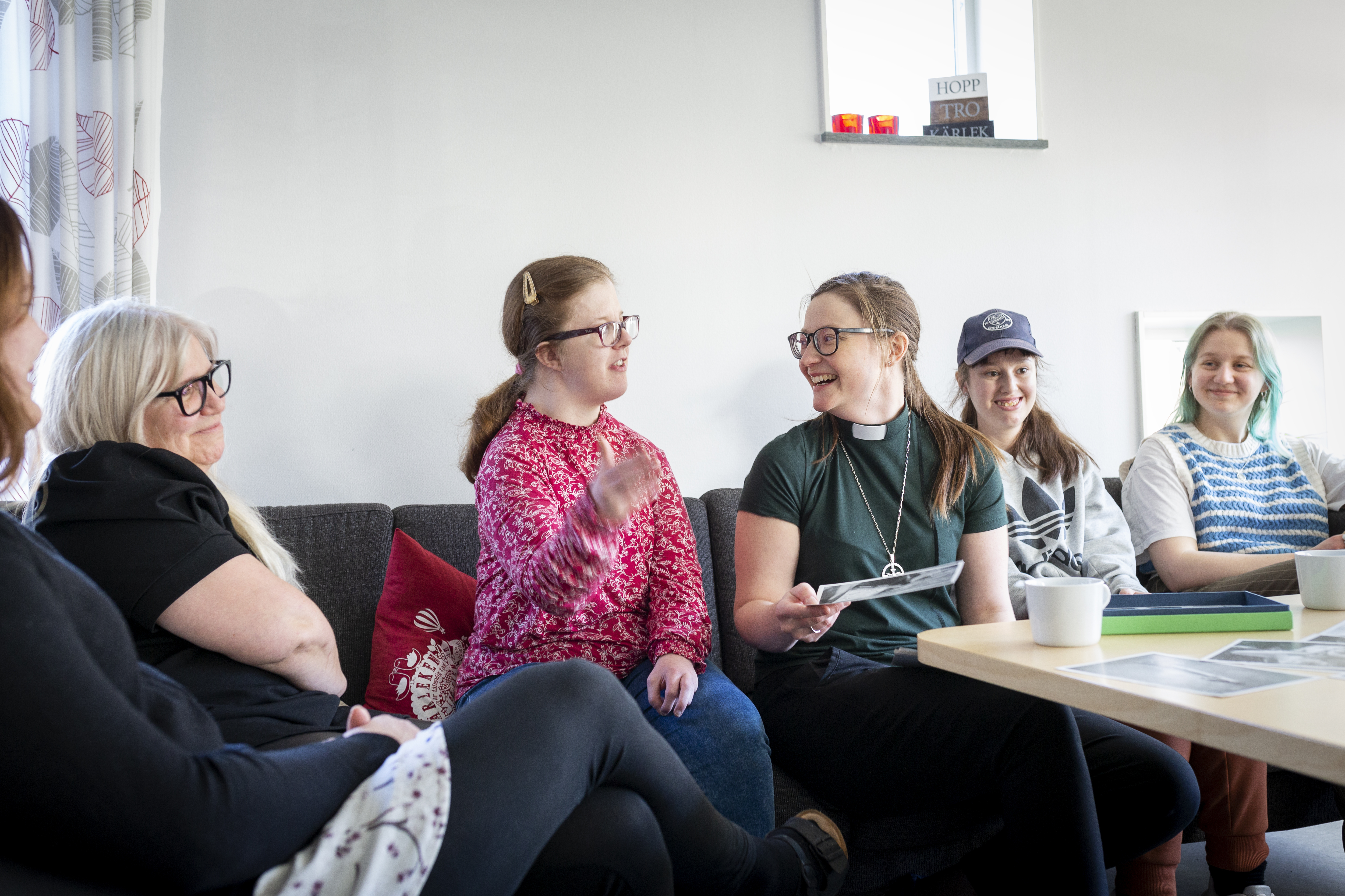 Ett gäng kvinnor i olika åldrar och en kvinnlig diakon sitter i en soffa och skrattar tillsammans.