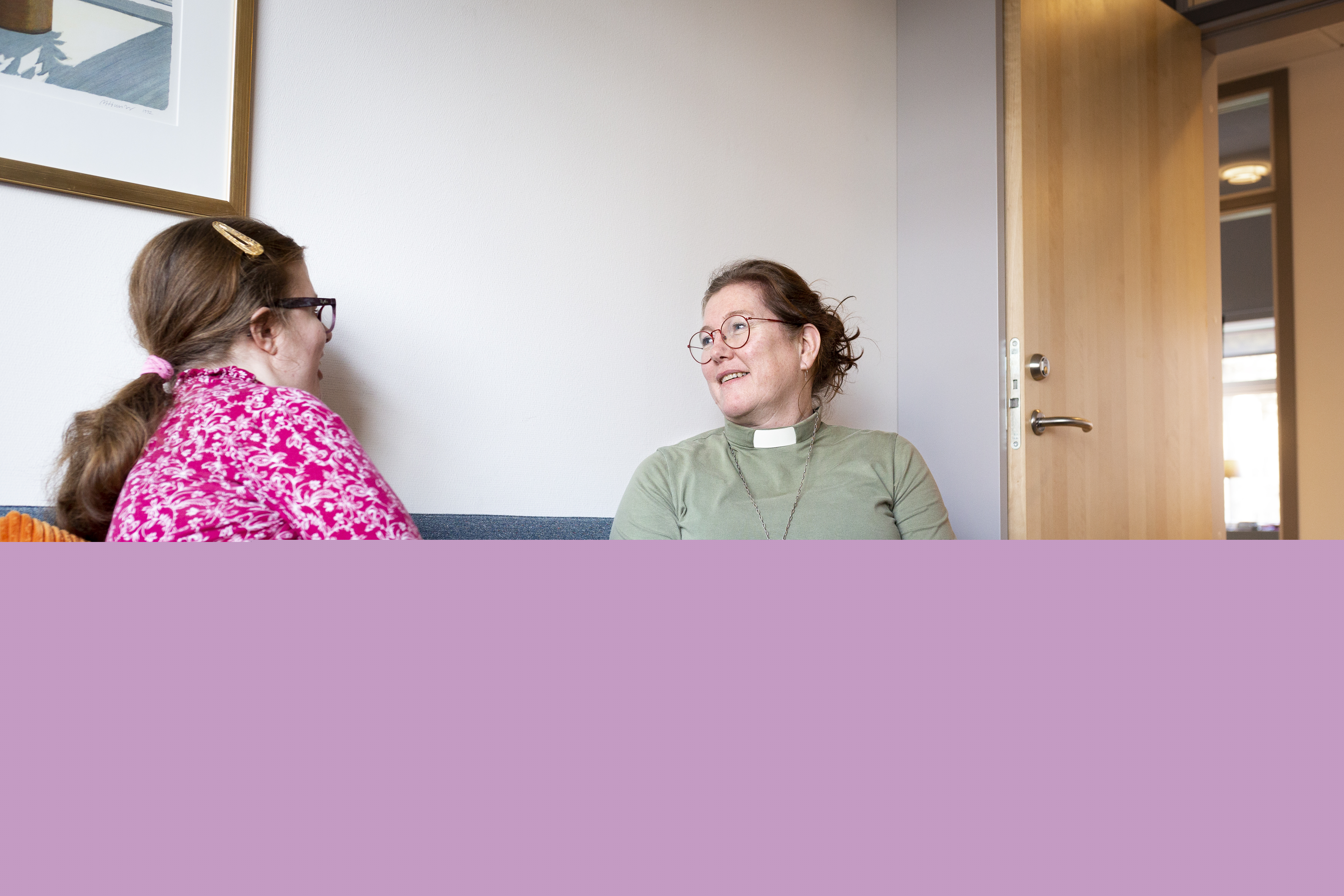 En kvinnlig diakon sitter och samtalar med en ung tjej i en soffa.