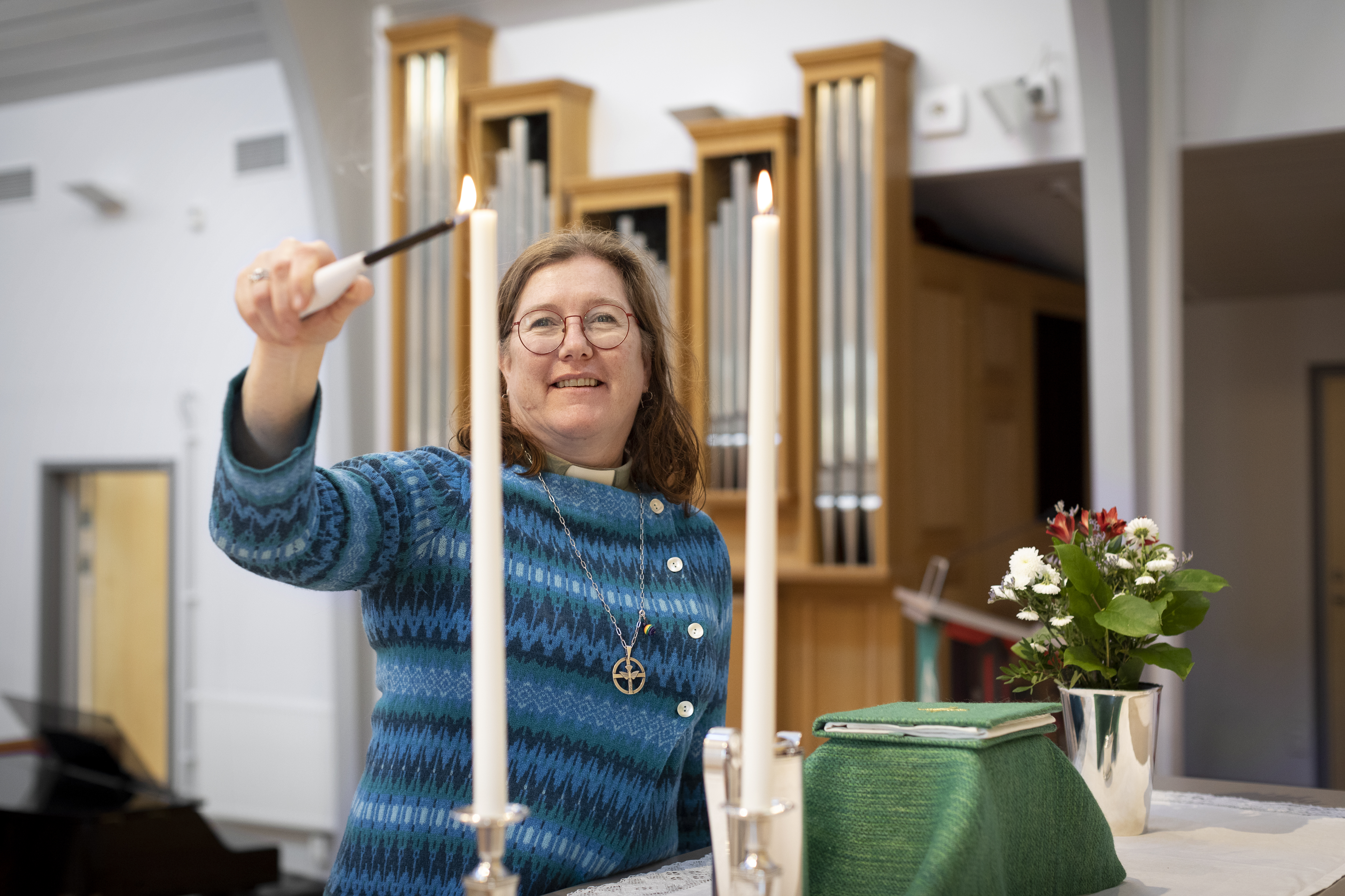 En kvinnlig diakon tänder två ljus på altaret.